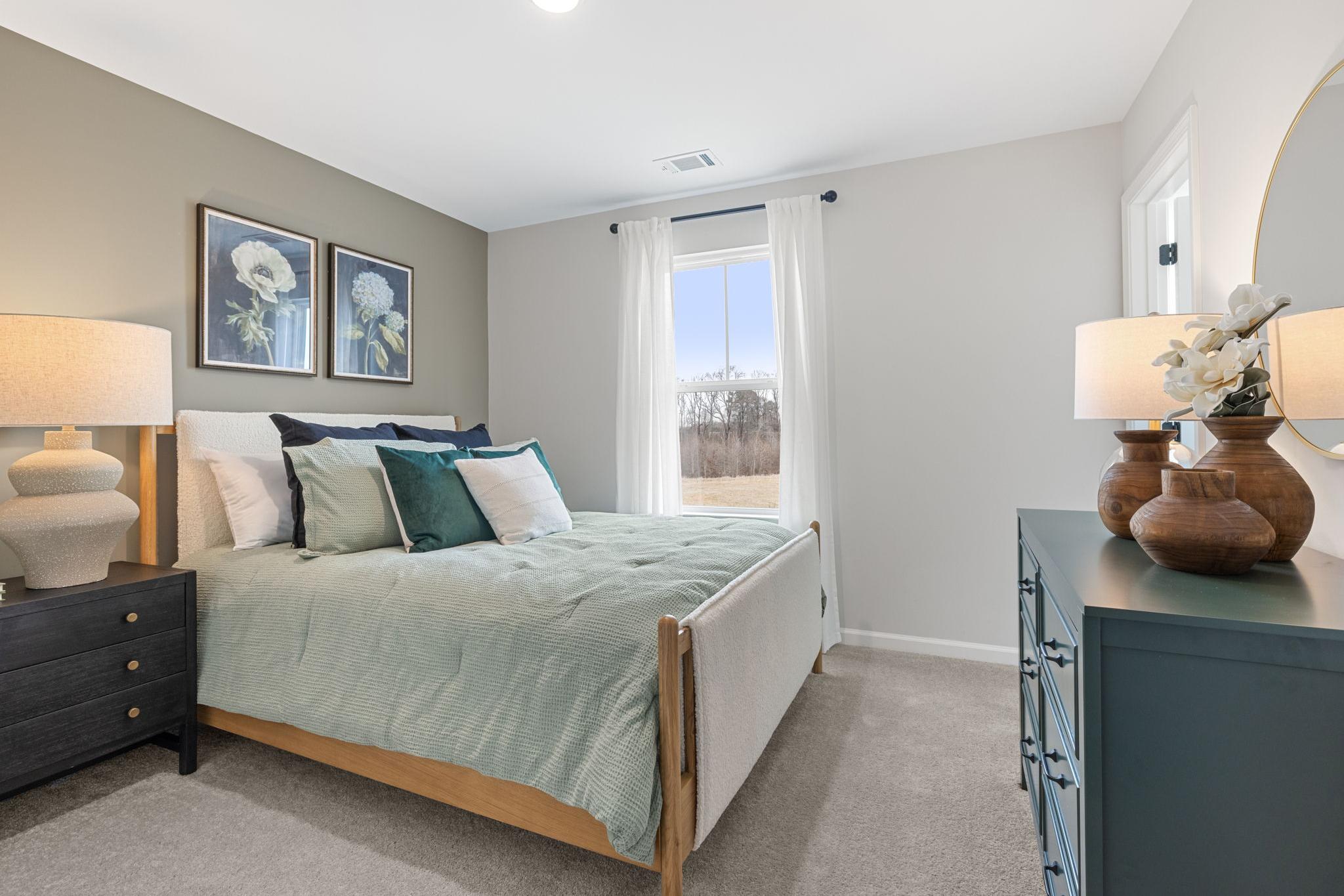 Cozy bedroom at Links Crossing in Auburn Alabama with upholstered bed, teal pillows, gray walls, floral art, and window view