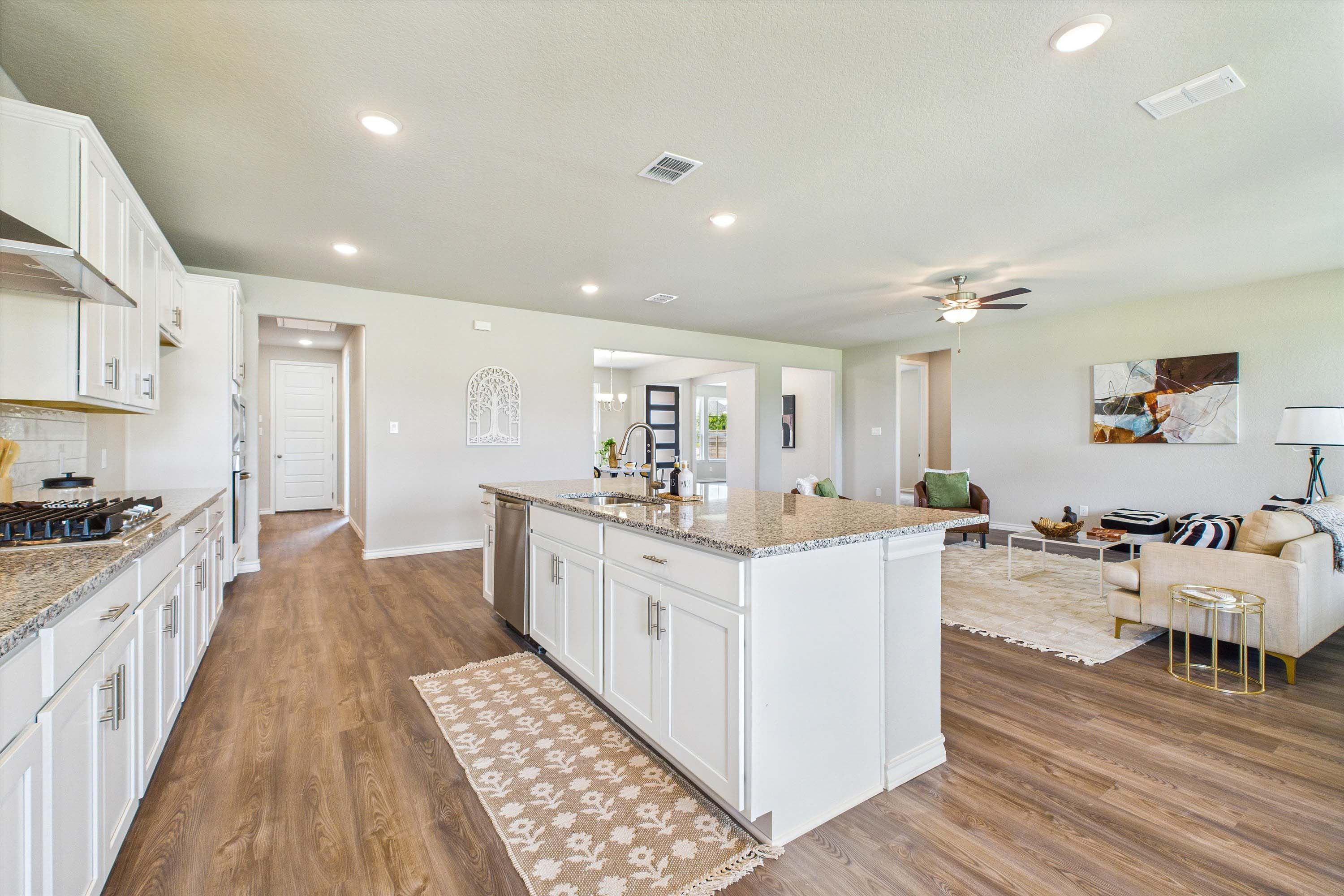 Open-concept kitchen and living area in The Foster featuring white cabinetry, granite countertops, and spacious layout.