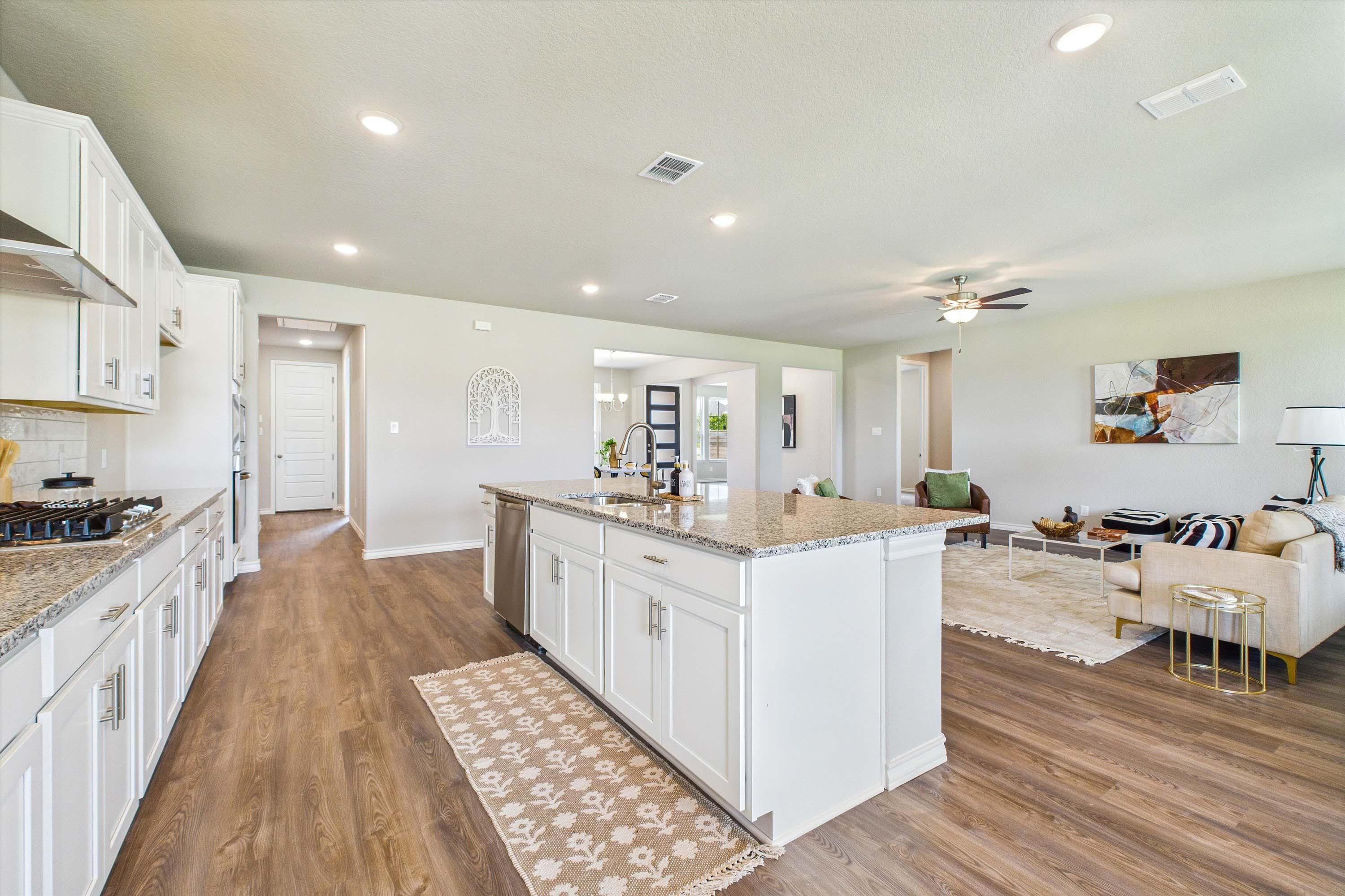 Open-concept kitchen and living area in The Foster featuring white cabinetry, granite countertops, and spacious layout.