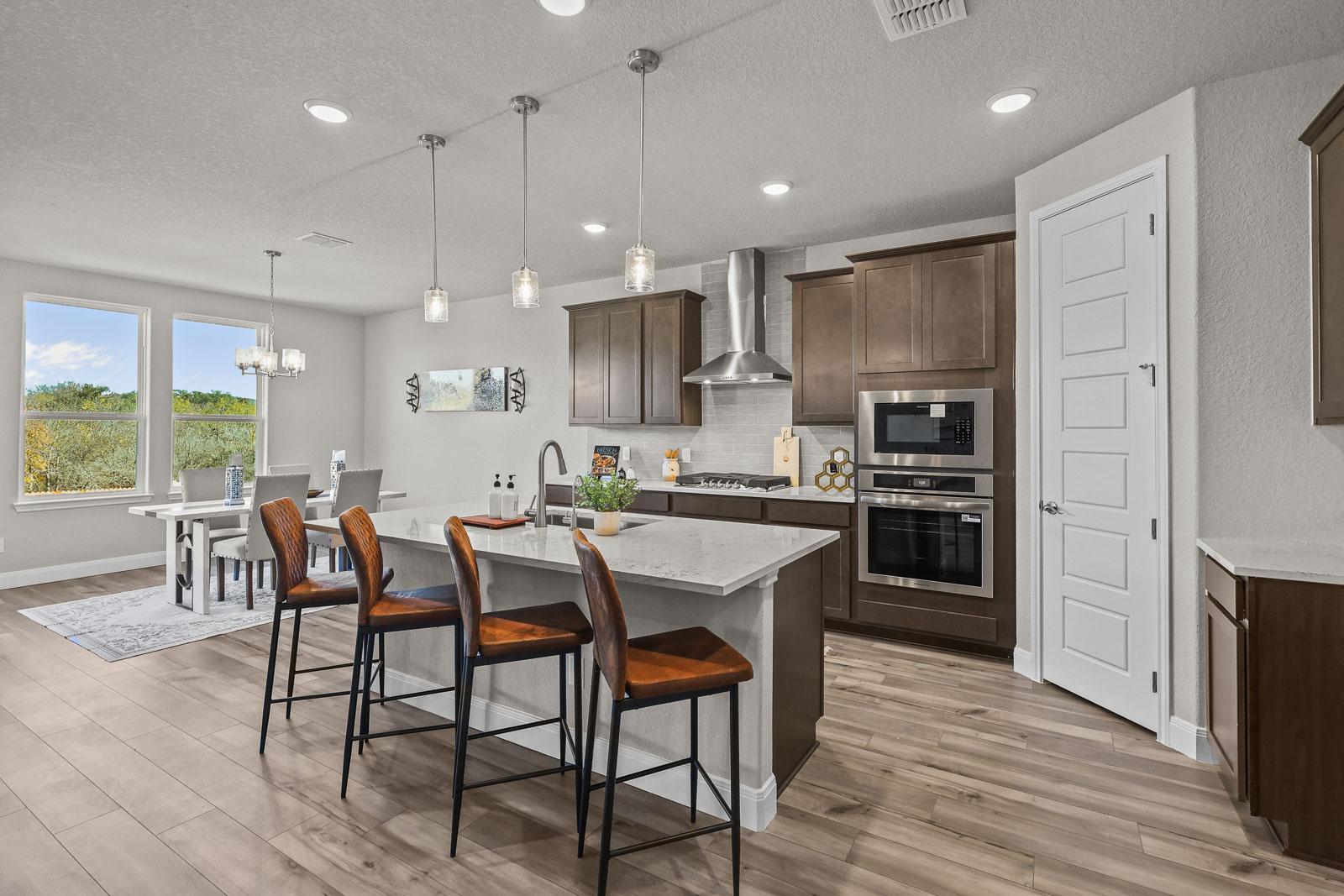 Modern kitchen in The Jennings G featuring a large island, stainless steel appliances, and an adjacent dining area.