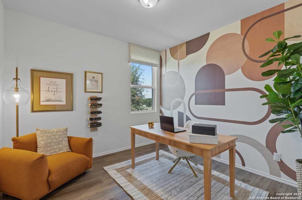 Modern home office with wooden desk, laptop, orange armchair, potted plant, and abstract terracotta wall art in Davidson Homes The Daphne J, Elmendorf, Texas