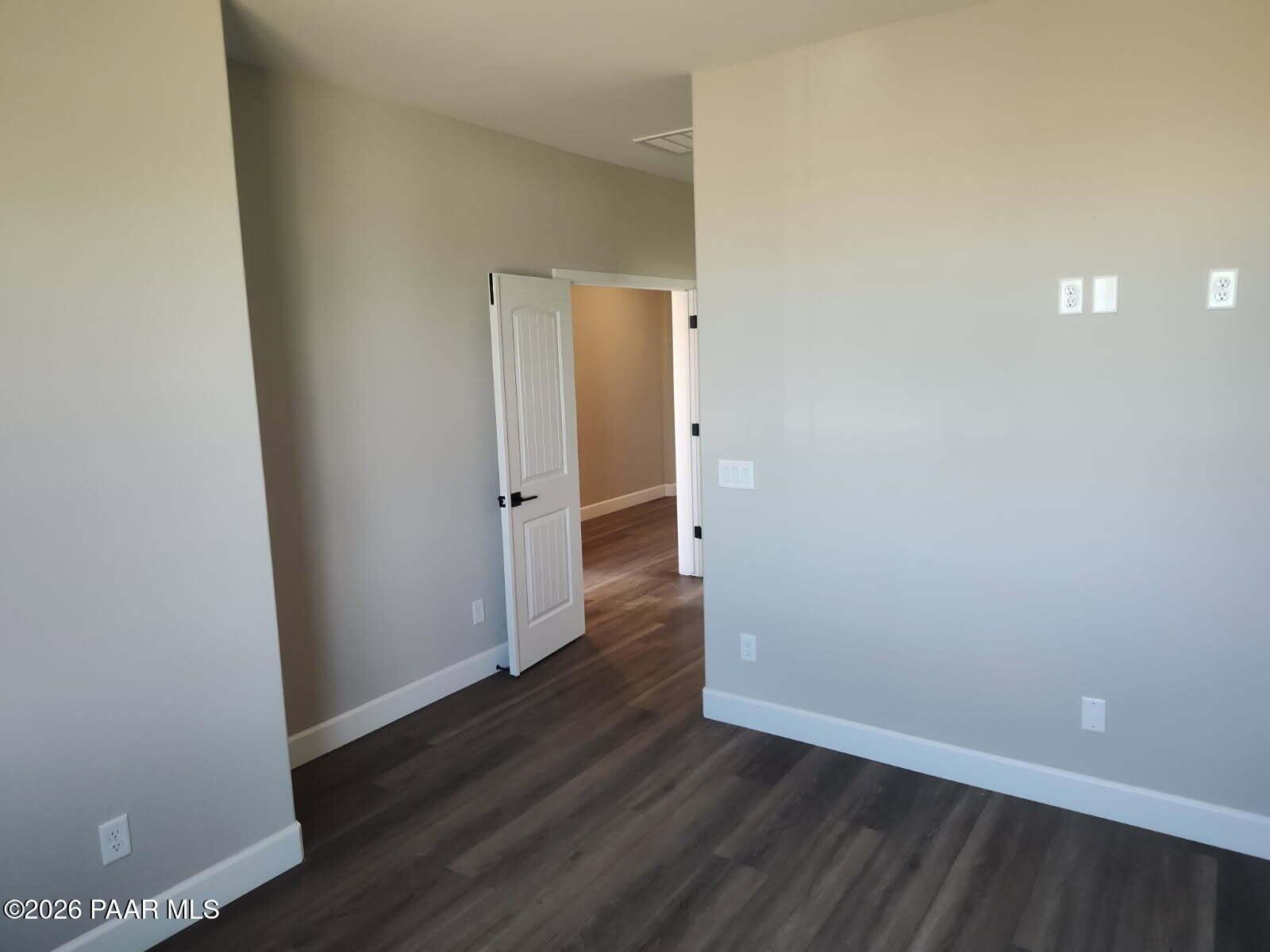 Spacious empty bedroom with beige walls, dark laminate flooring, open white door to hallway in Davidson Homes The Harmony C, Prescott Valley