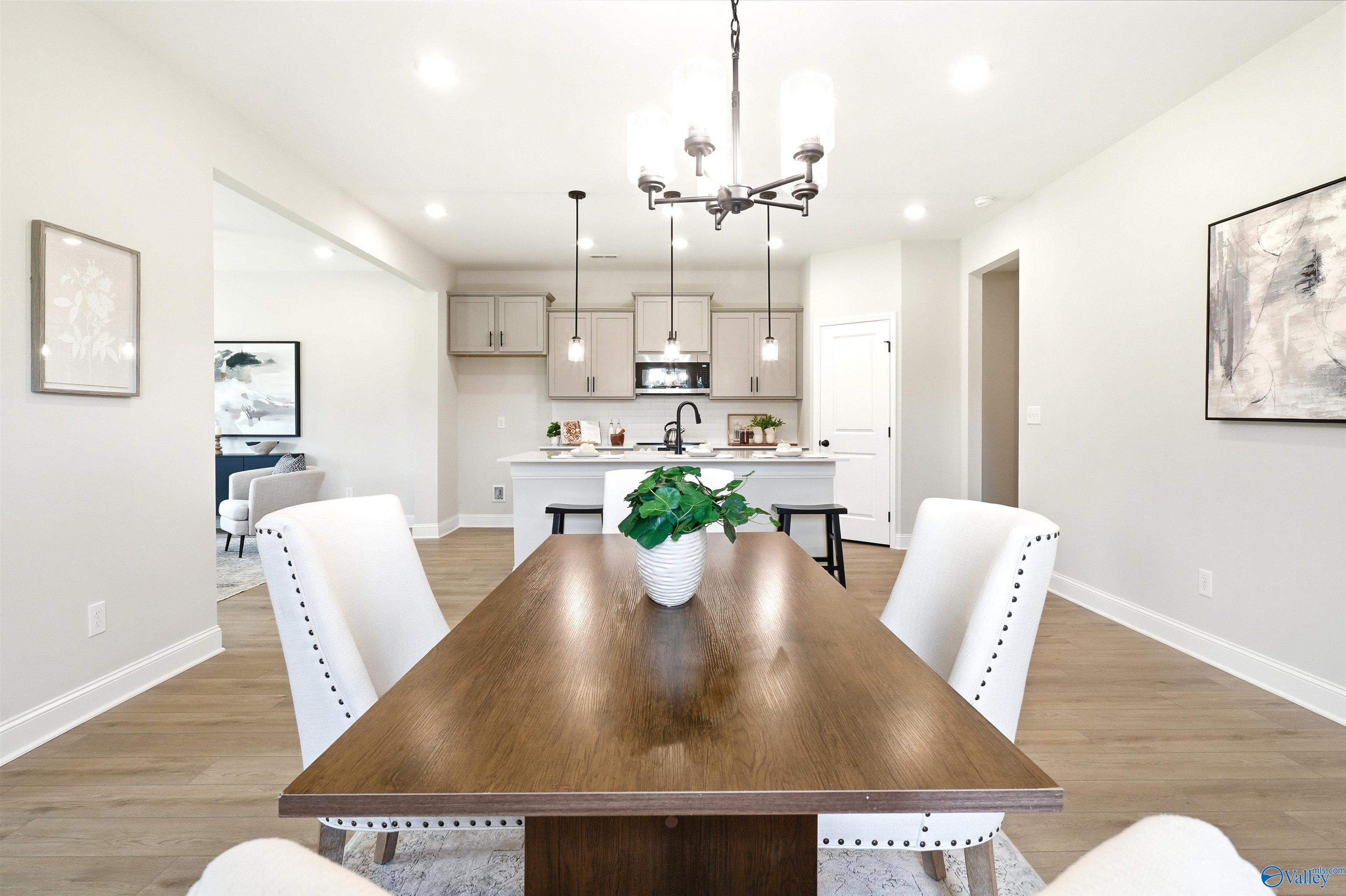 Elegant dining area with wood table and white chairs overlooking kitchen island in Davidson Homes Russell A plan, Huntsville, AL