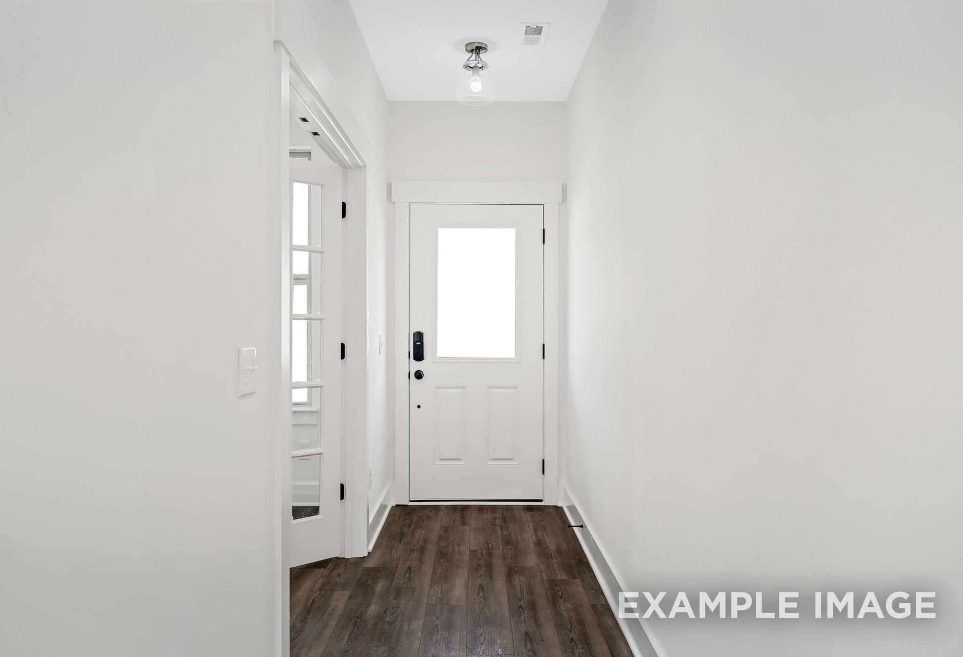 Spacious entry hallway in The Logan A featuring white paneled doors, hardwood floors, and modern lighting by Davidson Homes