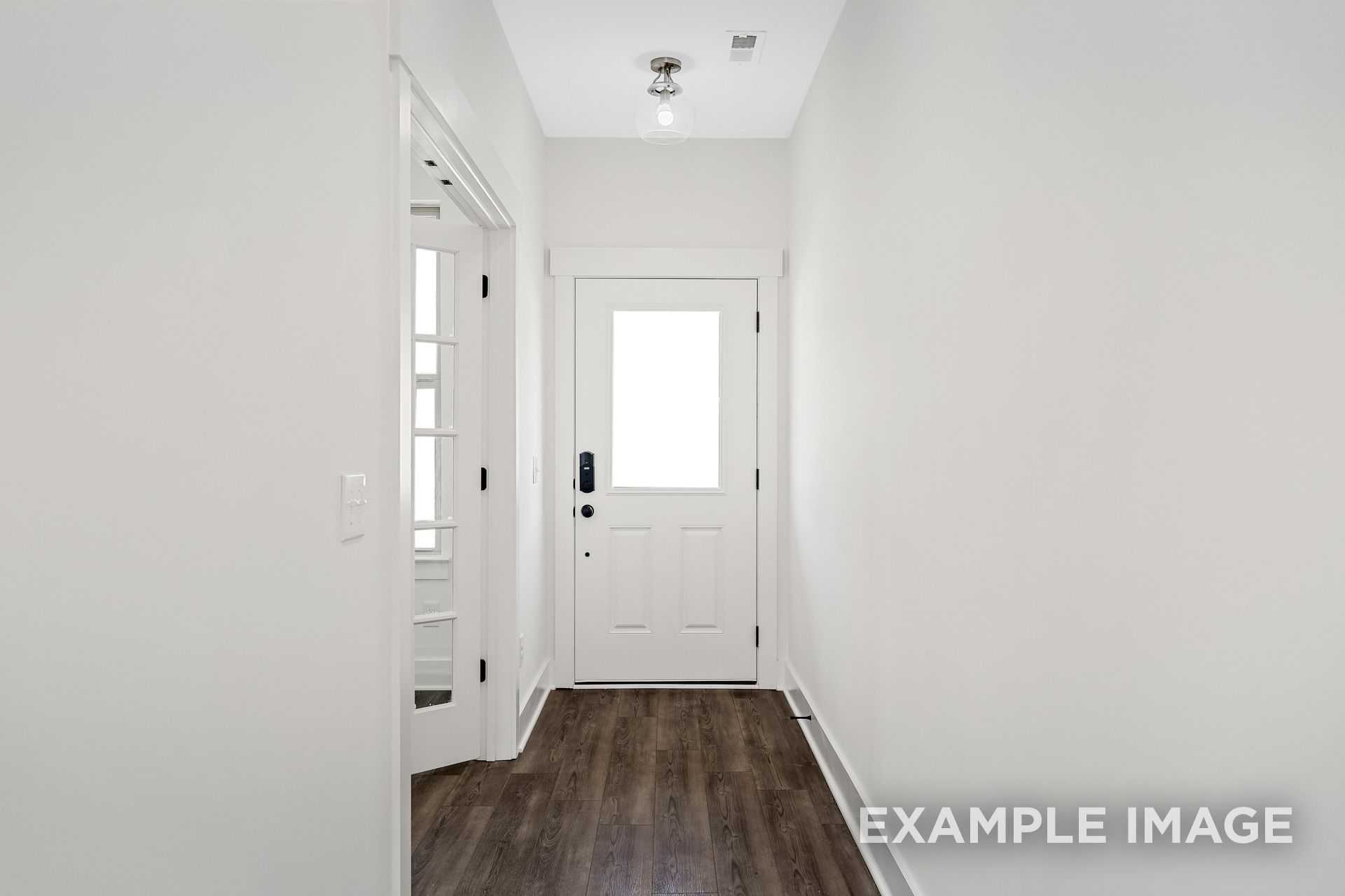 Bright hallway in The Logan B home featuring white walls, hardwood floors, and paneled front door