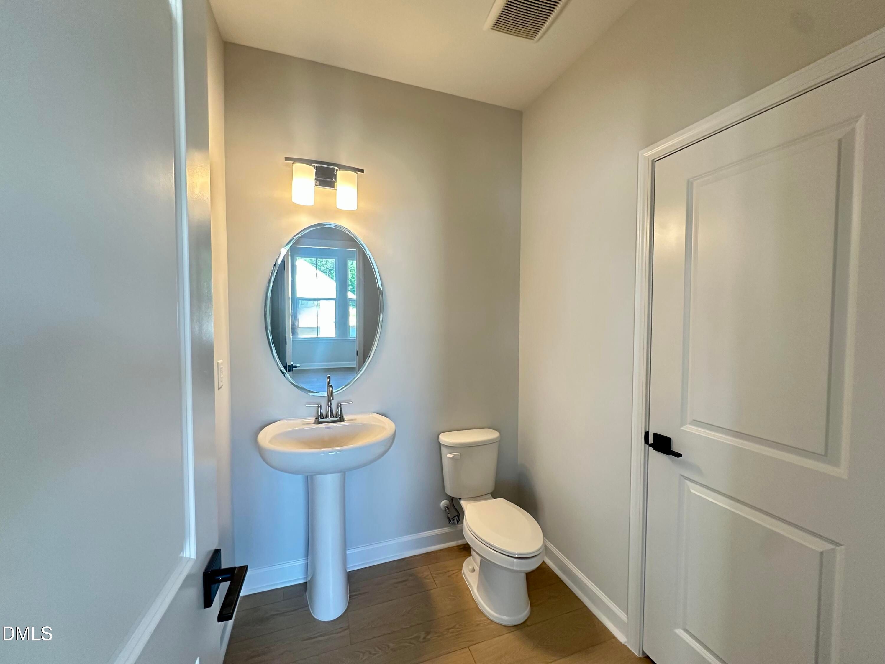 Modern powder room with pedestal sink, oval mirror, toilet, and hardwood floors in Davidson Homes The Avery, Knightdale, NC