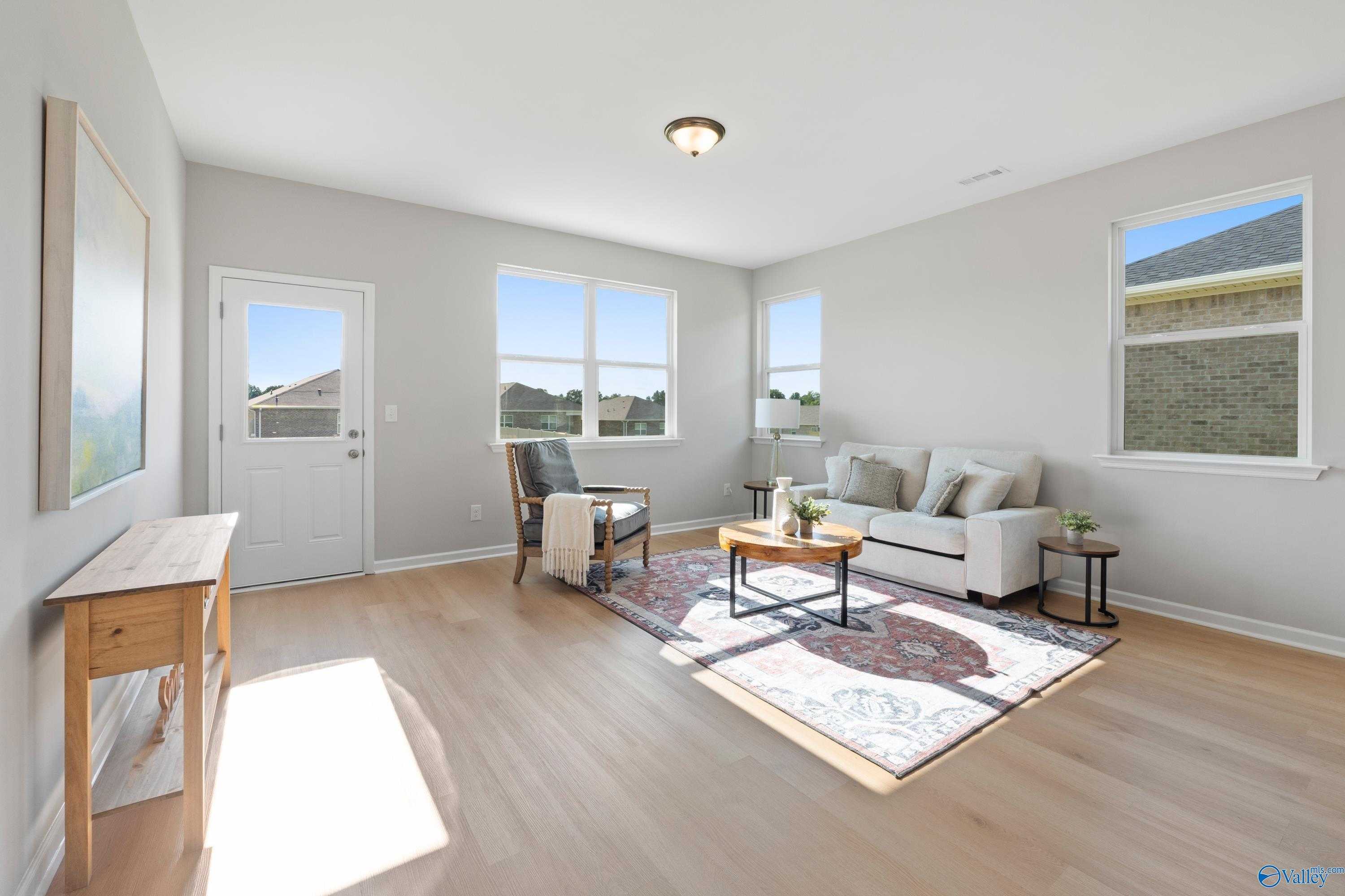 Bright living room with gray walls, large windows, beige sofa, hardwood floors, and area rug in Davidson Homes The Aurora, Fayetteville, TN
