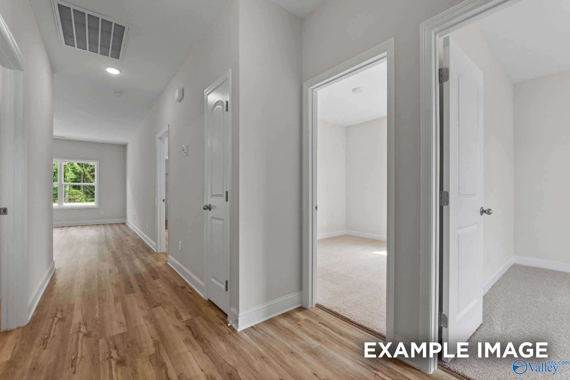 Bright hallway with hardwood floors, white doors, and empty bedrooms in Davidson Homes The Butler, Toney Alabama