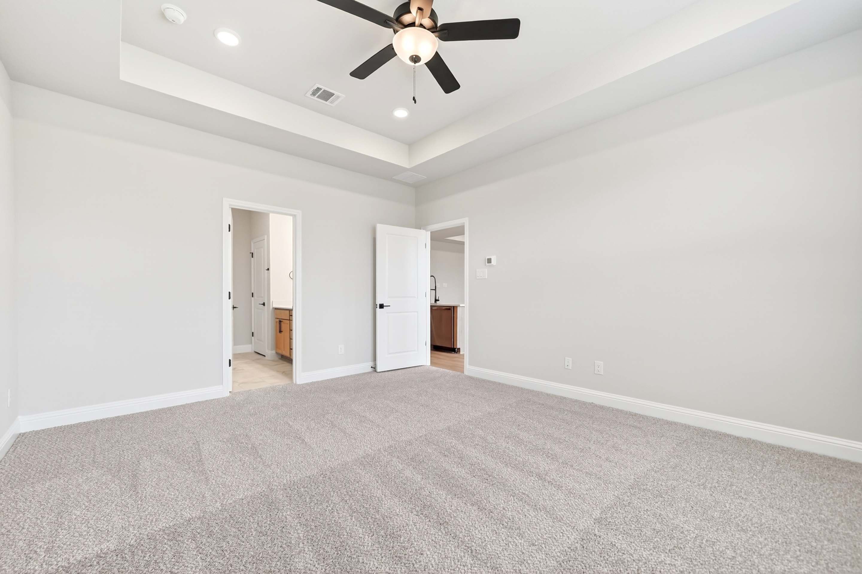 Spacious master suite in The Holly N floor plan featuring a tray ceiling, ceiling fan, and plush carpeting.