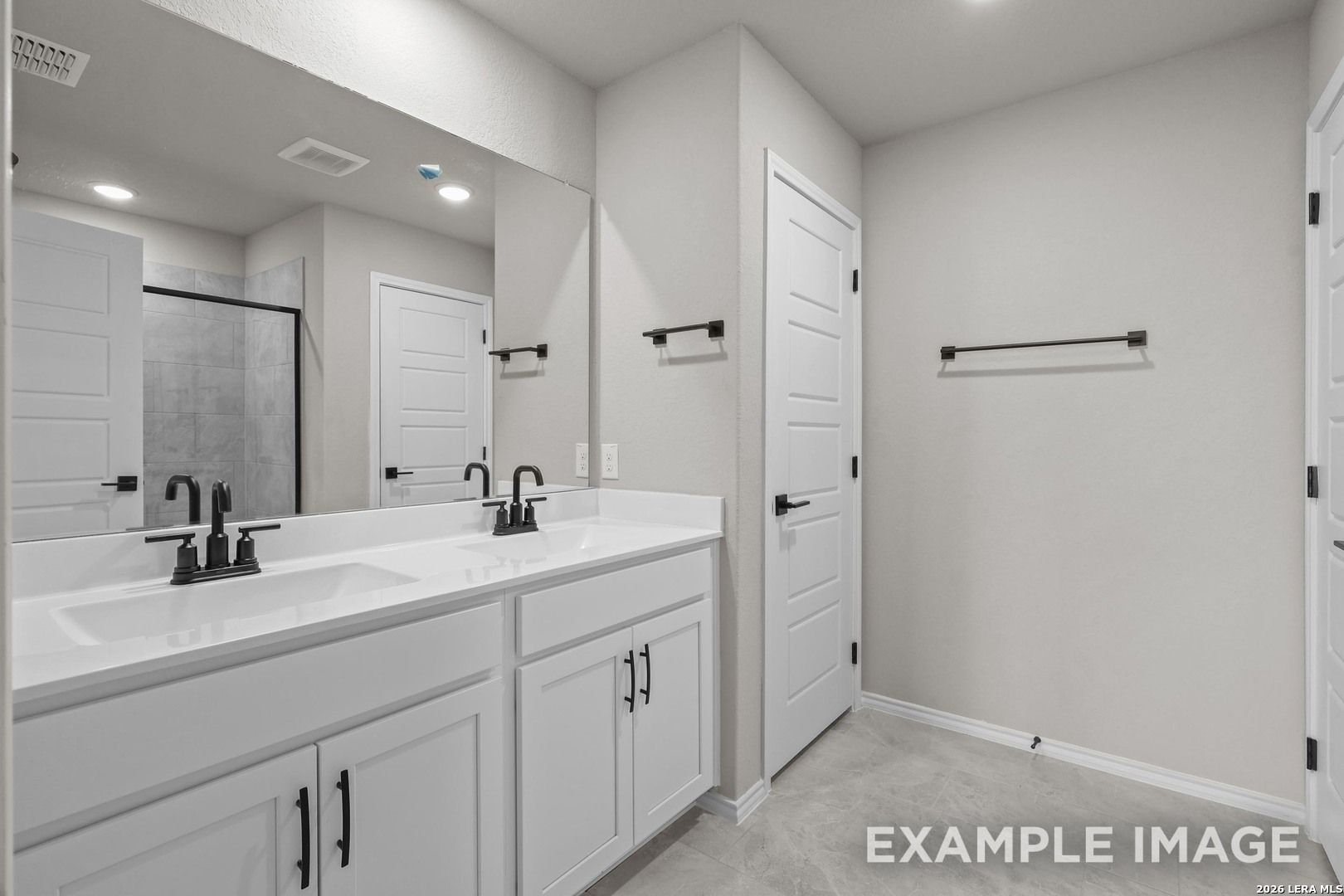 Dual-sink bathroom with white vanity, matte black fixtures and tiled walk-in shower in The Murray H floor plan, Converse, TX