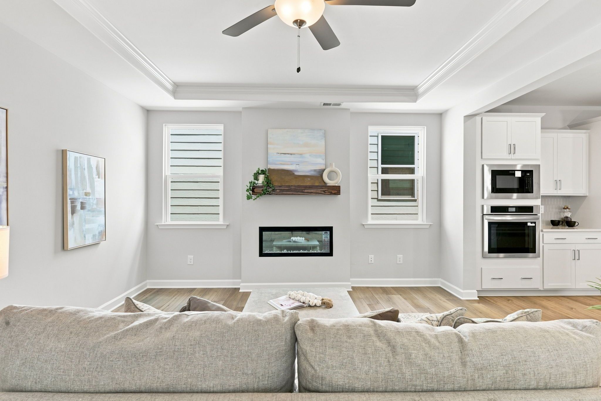 Open-concept living room in The Jordan A featuring a modern fireplace, tray ceiling, and adjacent gourmet kitchen.