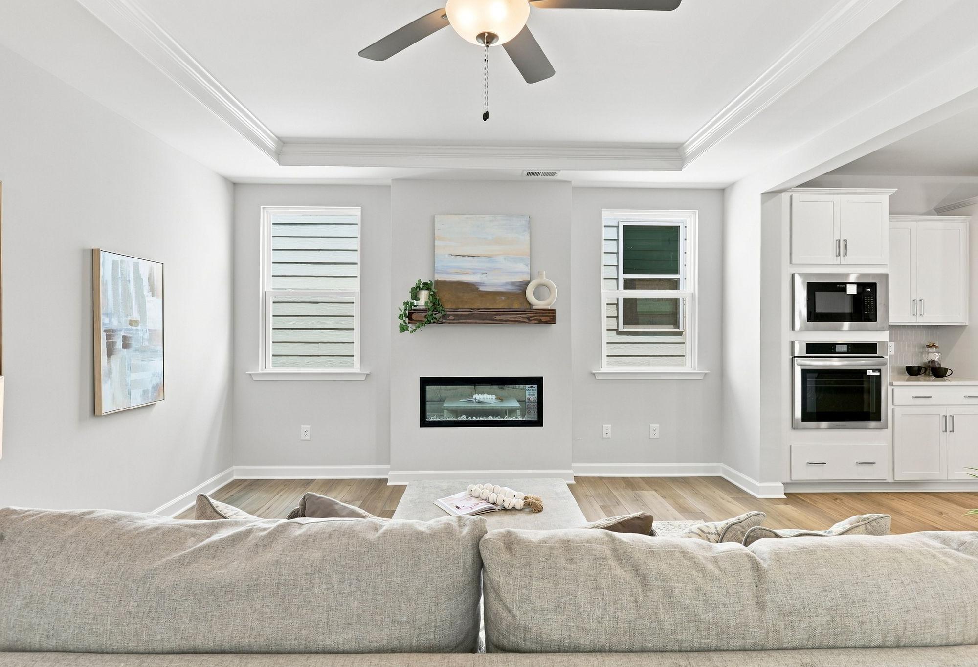Open-concept living room in The Jordan A featuring a modern fireplace, tray ceiling, and adjacent gourmet kitchen.