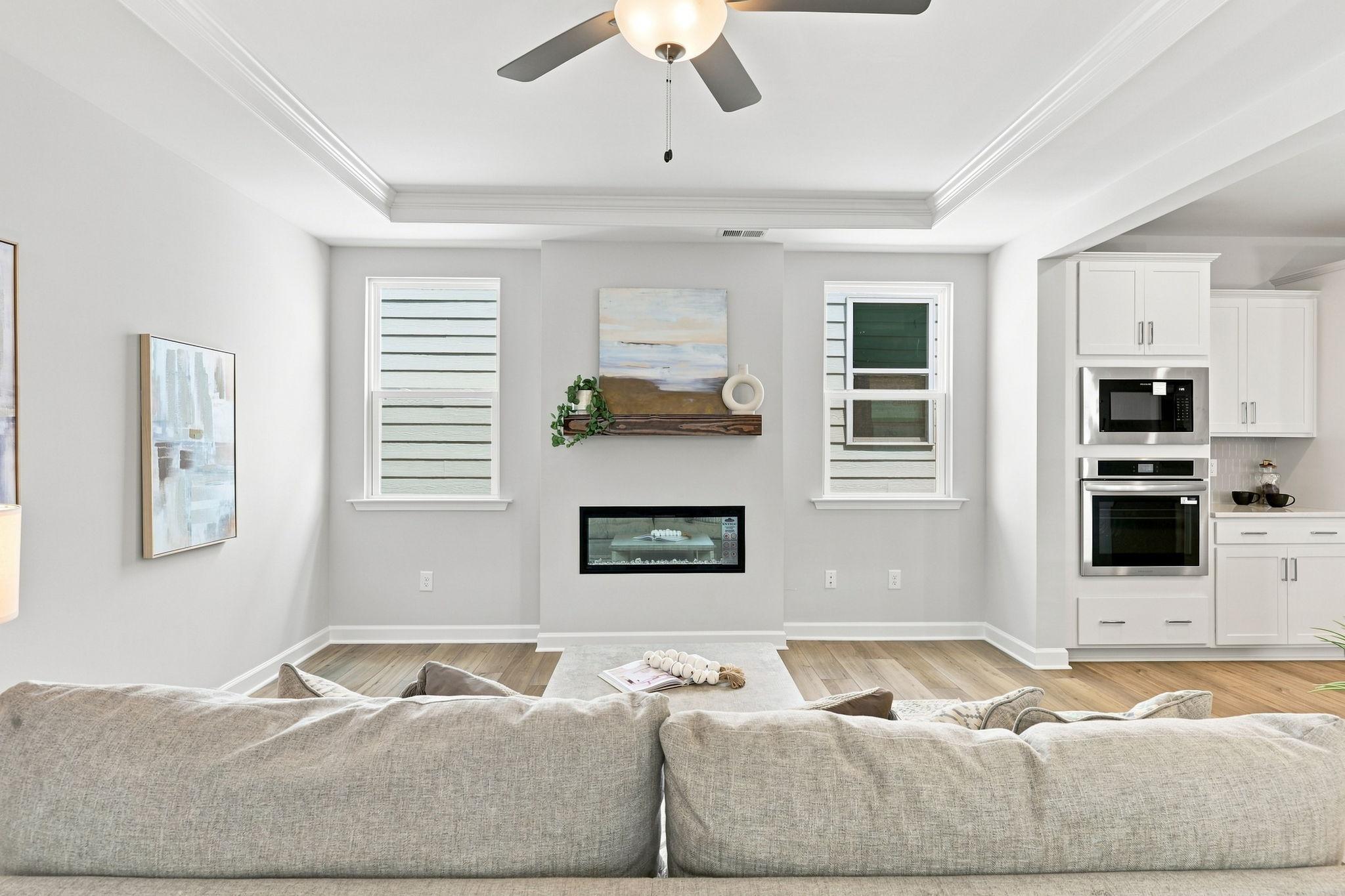 Open-concept living room in The Jordan A featuring a modern fireplace, tray ceiling, and adjacent gourmet kitchen.
