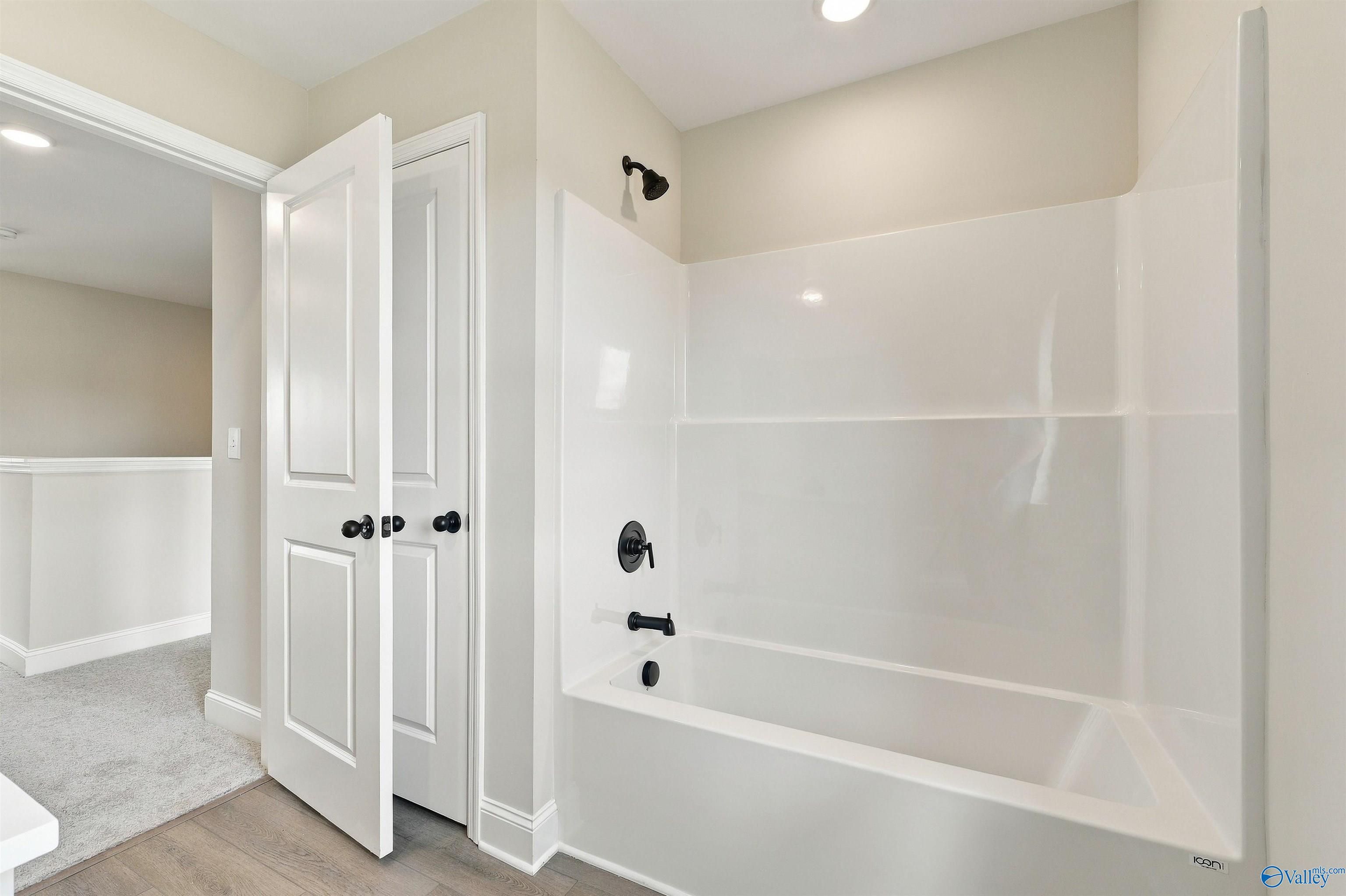 White tub-shower with matte black fixtures beside double-door closet in bathroom of Davidson Homes The Shelby A, Athens, Alabama