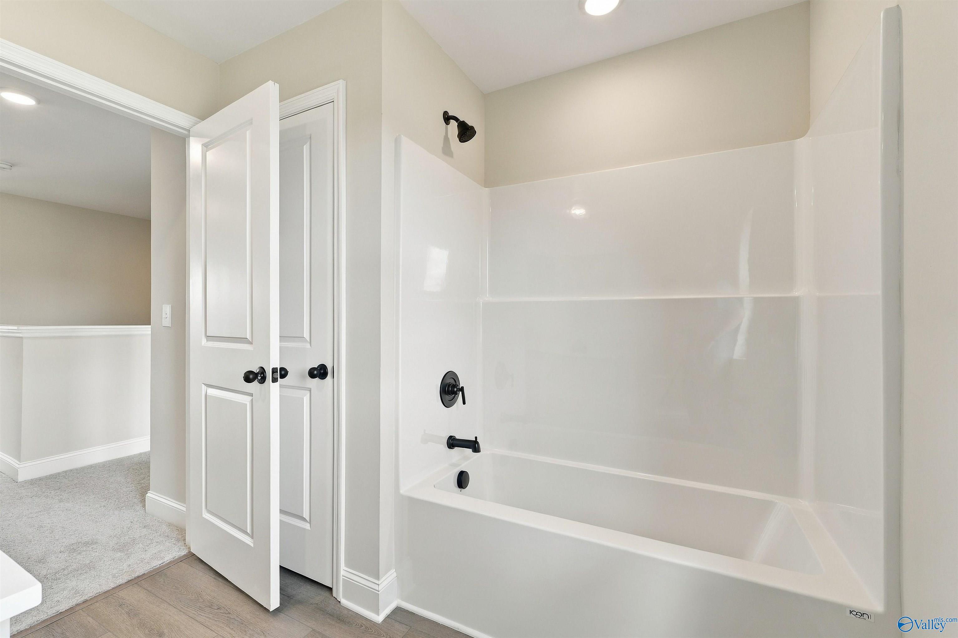 White tub-shower with matte black fixtures beside double-door closet in bathroom of Davidson Homes The Shelby A, Athens, Alabama