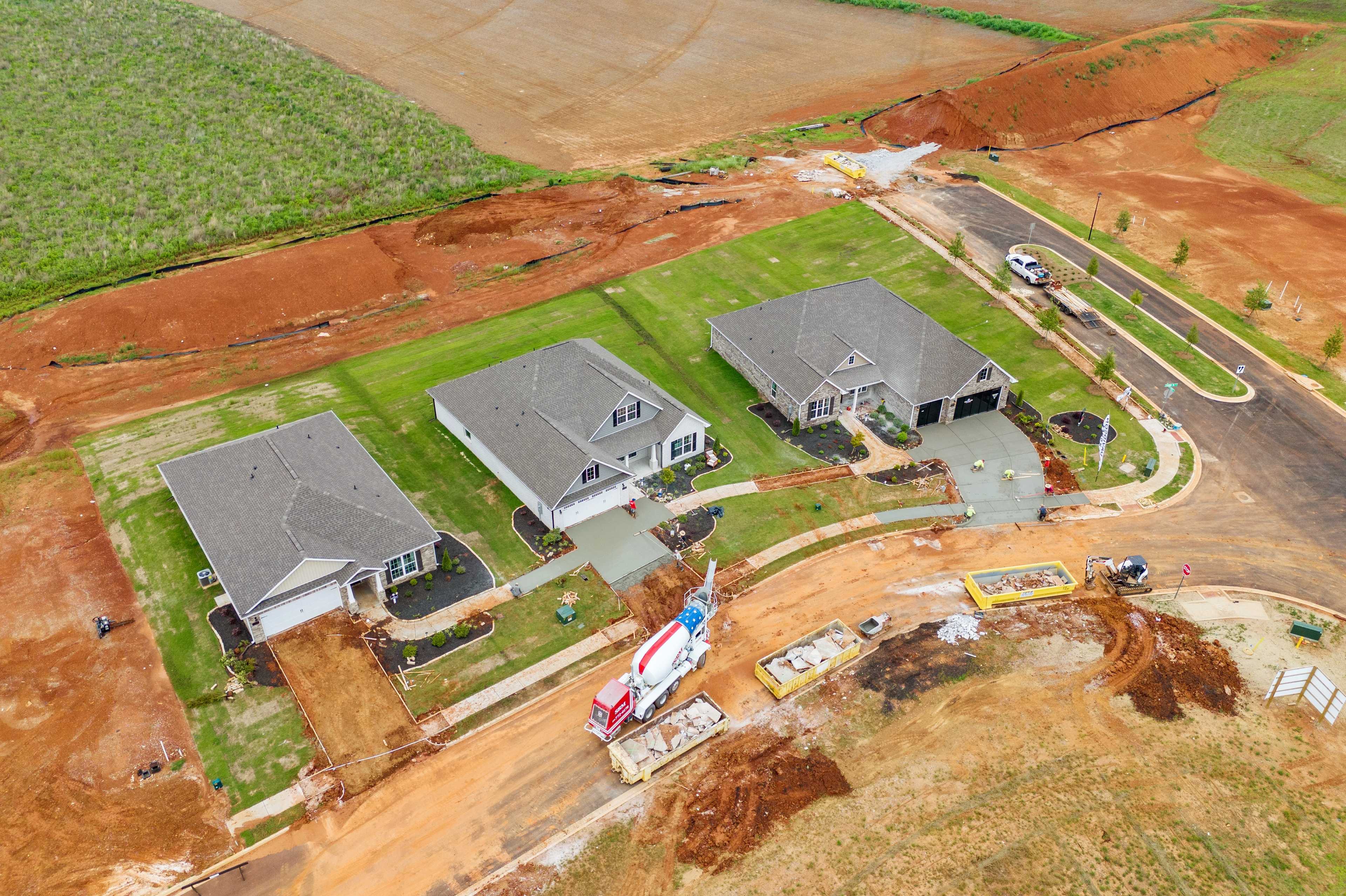 Aerial view of three new homes under construction at Creekside in Harvest, Alabama with concrete mixer truck and red clay fields