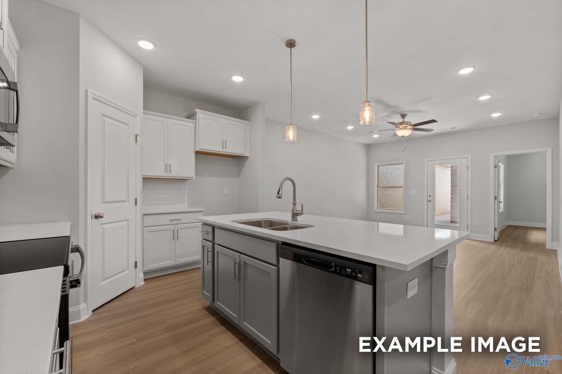 Modern open-concept kitchen with white cabinets, quartz island, stainless sink, and pendant lights in The Camilla B, Hartselle, AL