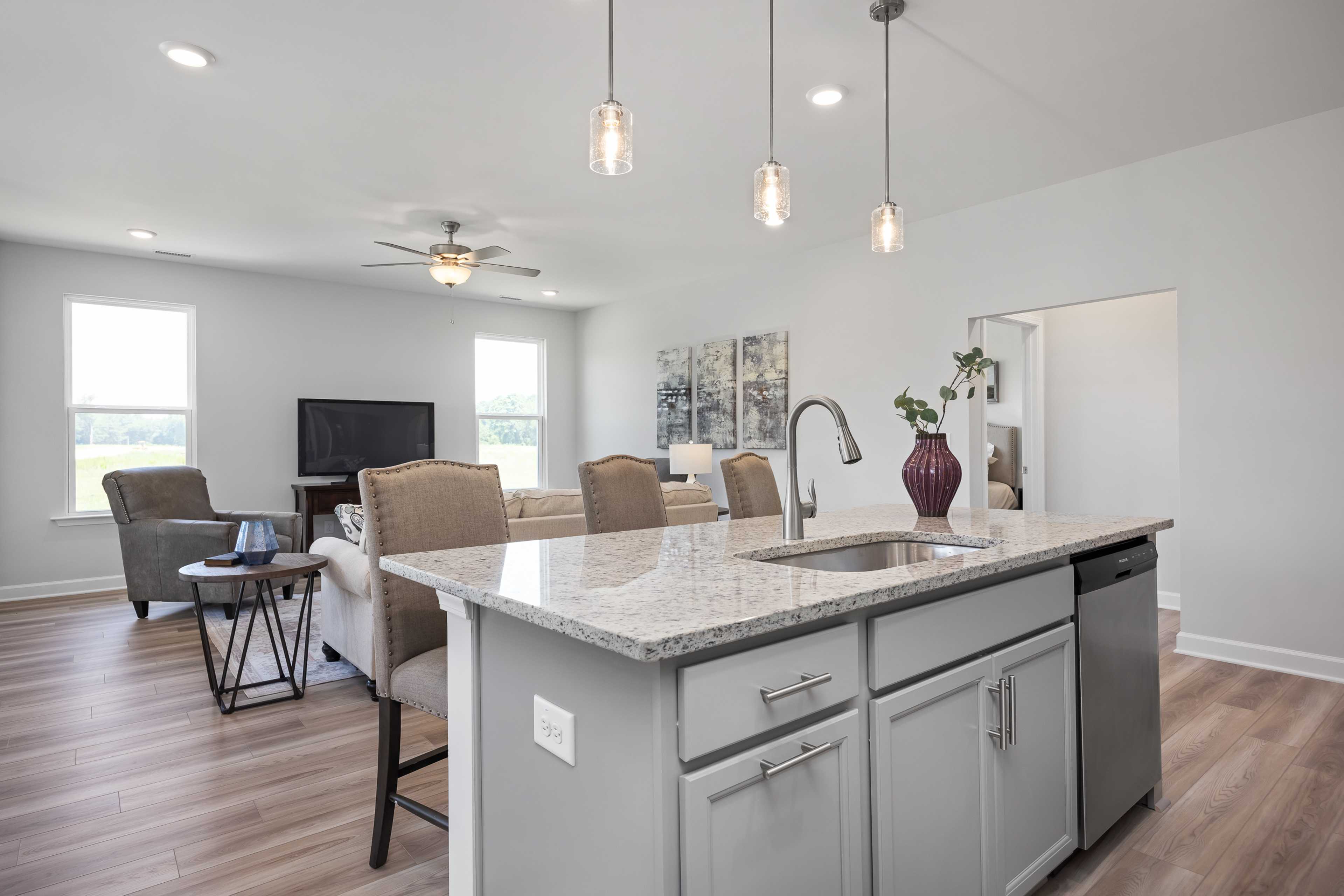 Open-concept kitchen and living room at Woodland Crossing in Zebulon NC with granite island, hardwood floors, pendant lights
