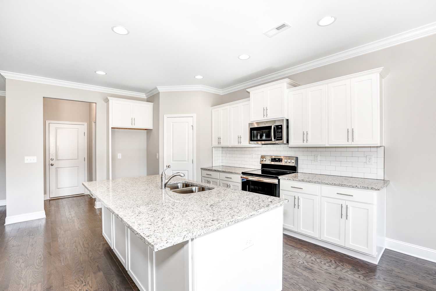 Bright open kitchen in The Montgomery featuring white shaker cabinets, granite island, subway tile backsplash