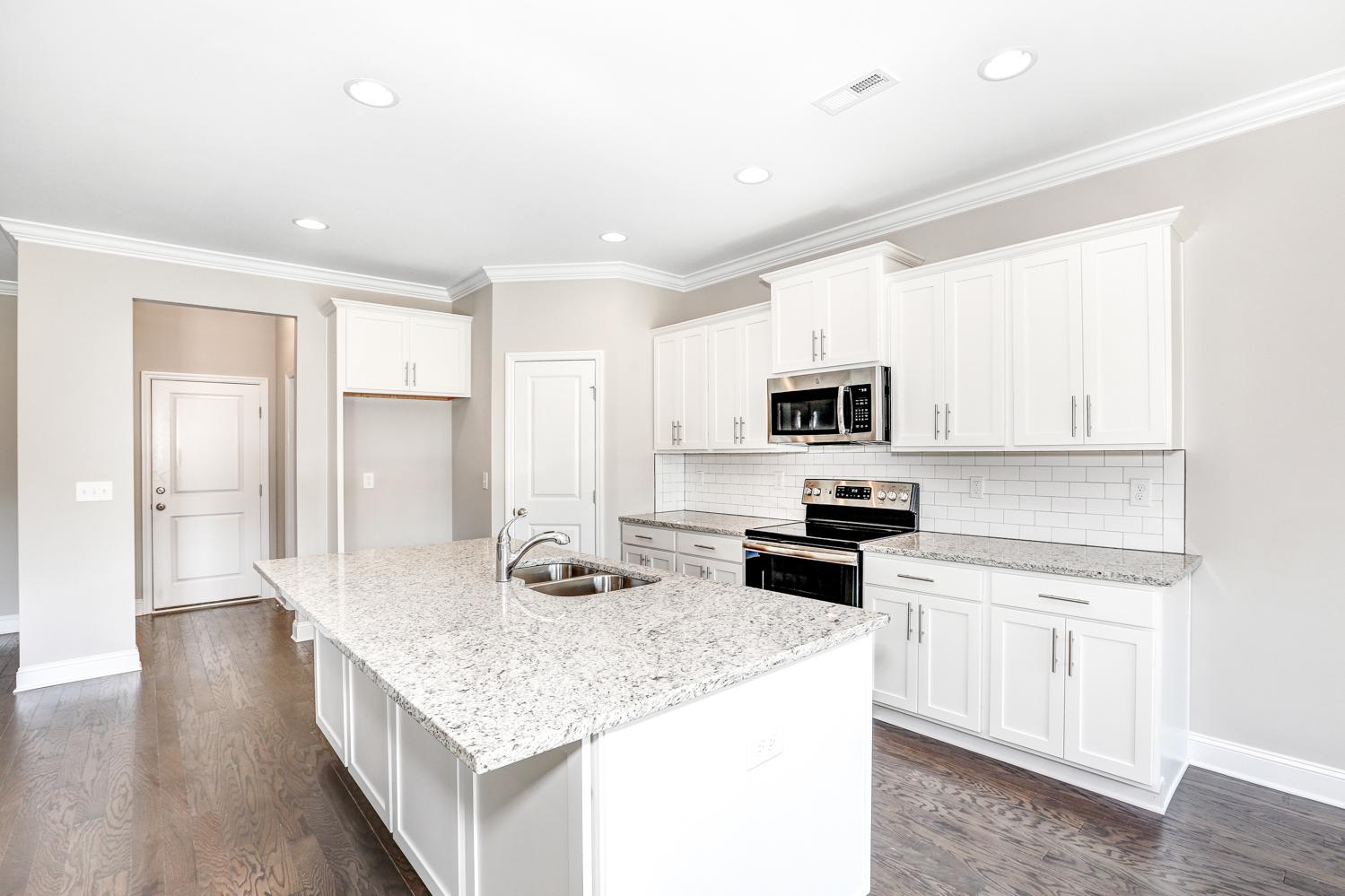 Bright open kitchen in The Montgomery featuring white shaker cabinets, granite island, subway tile backsplash