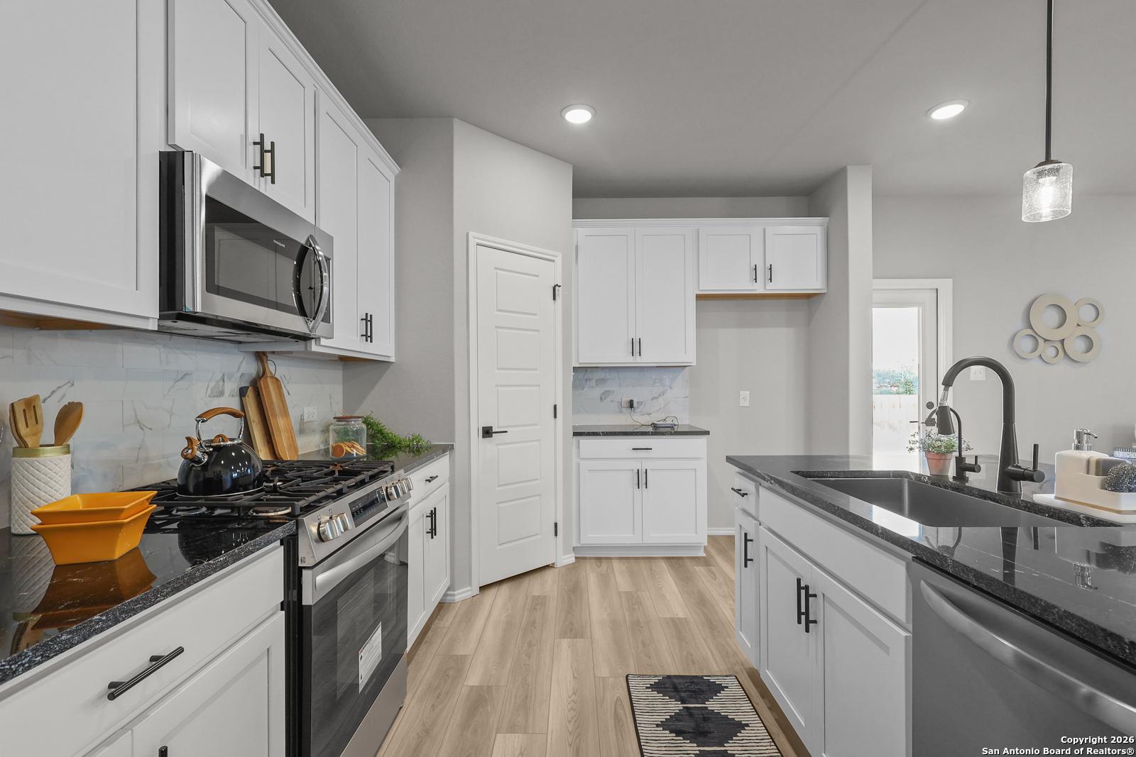 Modern white kitchen with stainless steel appliances, black granite island, and subway tile backsplash in Davidson Homes The Murray K, San Antonio