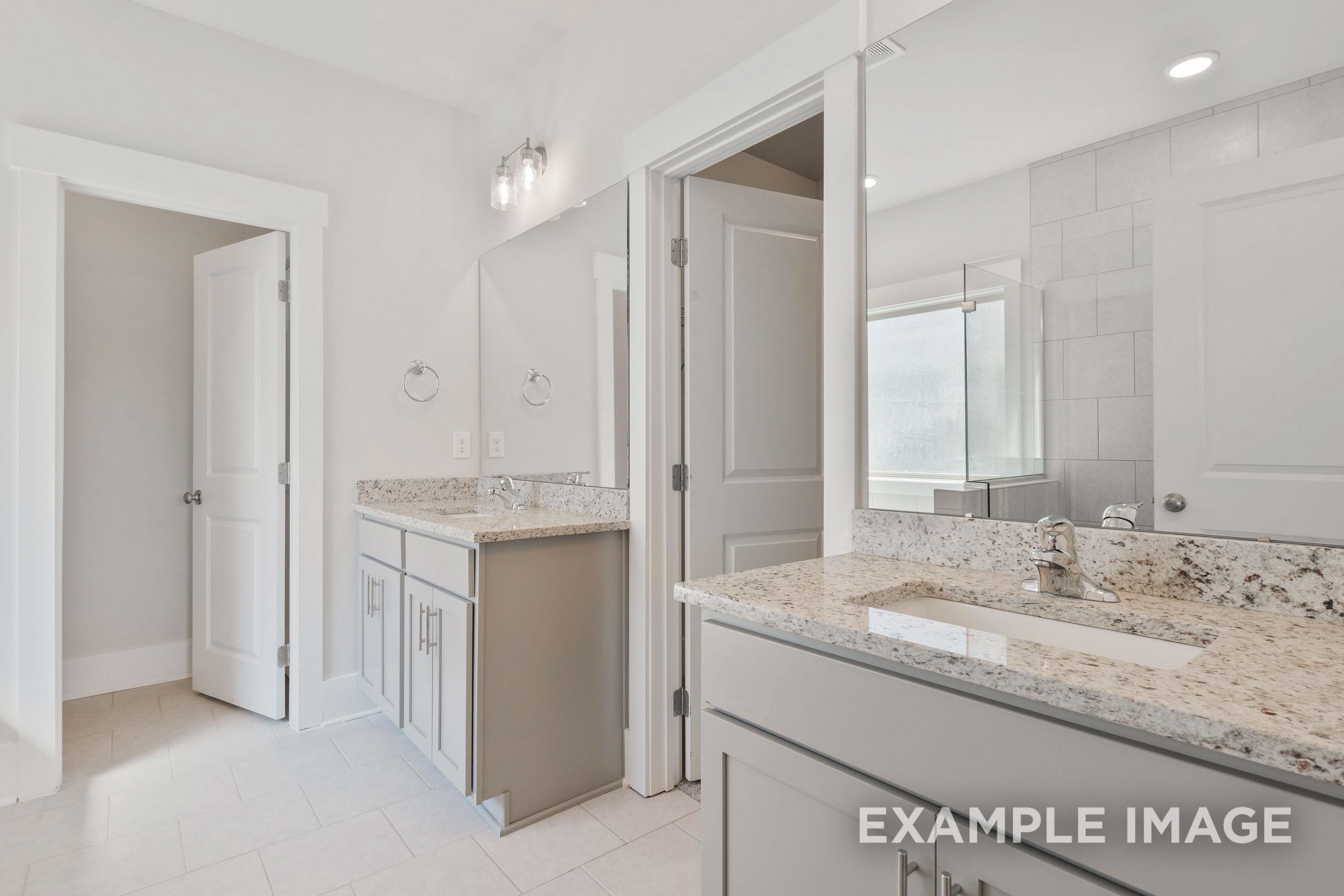 Spacious primary bathroom in The Richmond D featuring a double vanity with granite countertops and modern grey cabinetry.