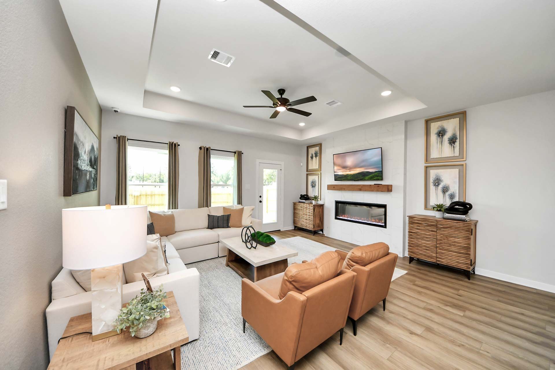 Modern living room at Enclave at Newport in Crosby, TX featuring a fireplace, tray ceiling, and stylish furniture.
