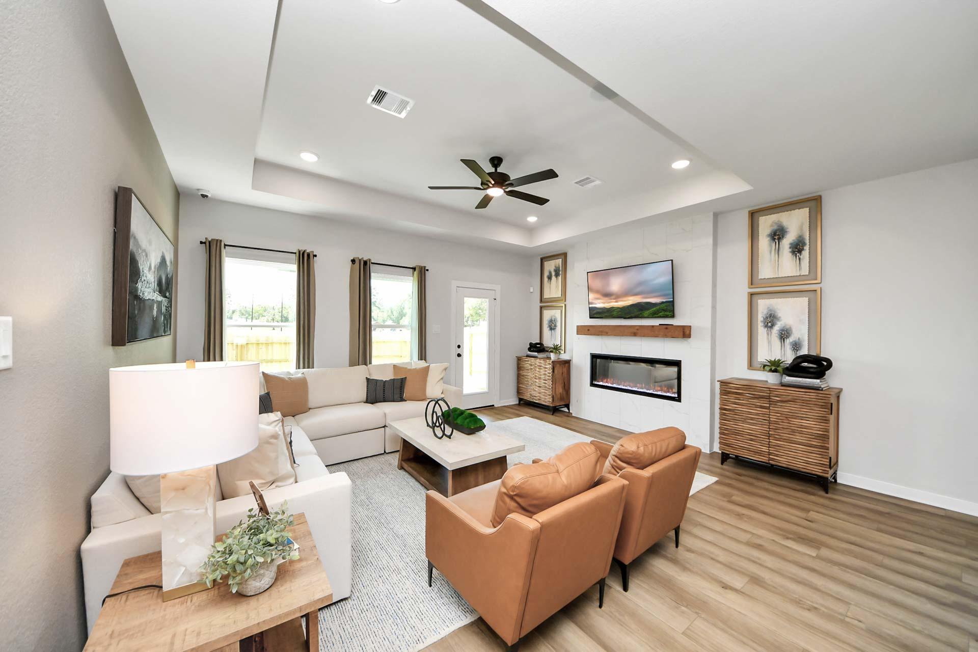 Modern living room at Enclave at Newport in Crosby, TX featuring a fireplace, tray ceiling, and stylish furniture.