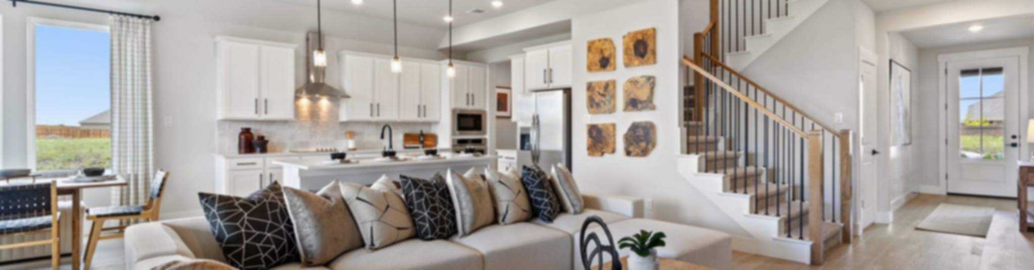 Open-concept living room and kitchen in new Anna home, white cabinets, beige sofa, wooden accents, staircase
