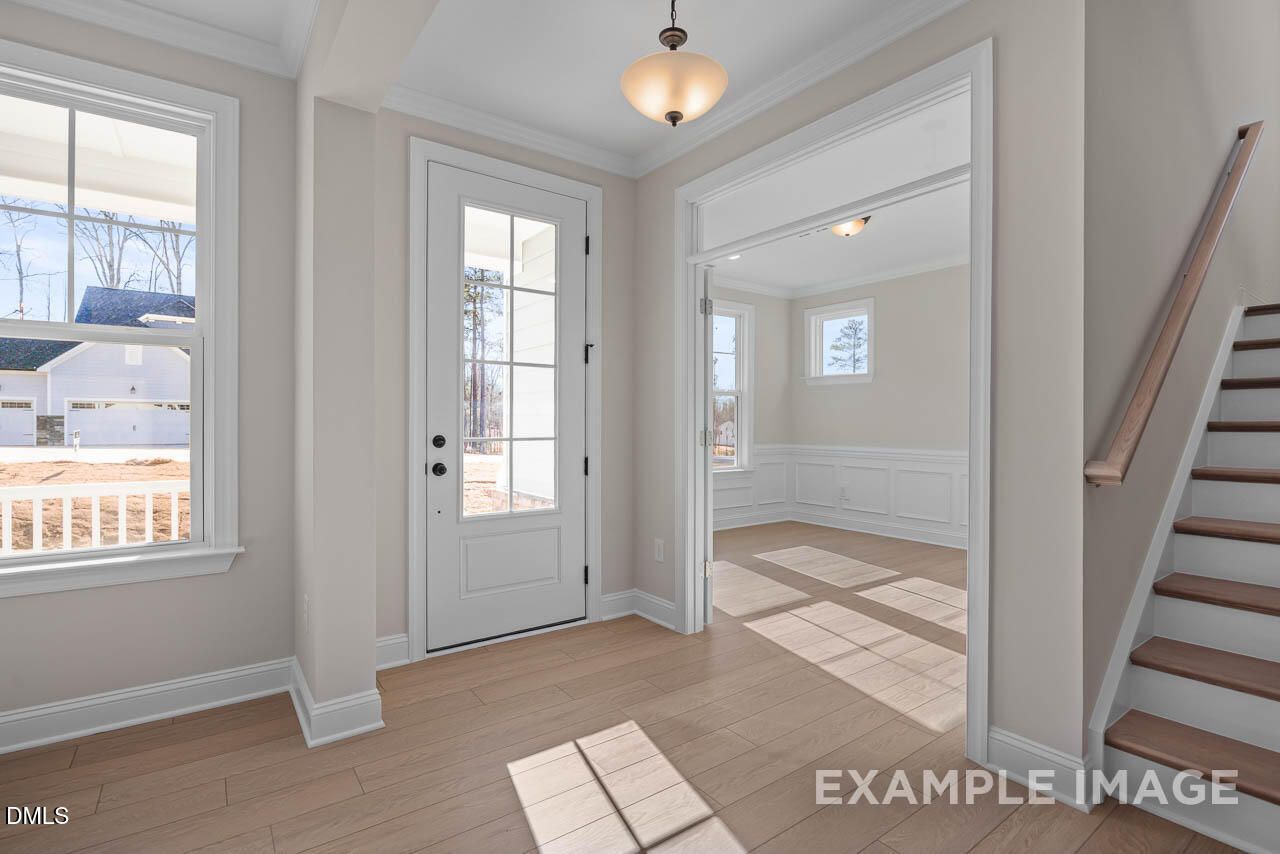 Bright entry foyer with hardwood floors, glass-front door, chandelier, and staircase in Davidson Homes The Crawford D, Angier, NC