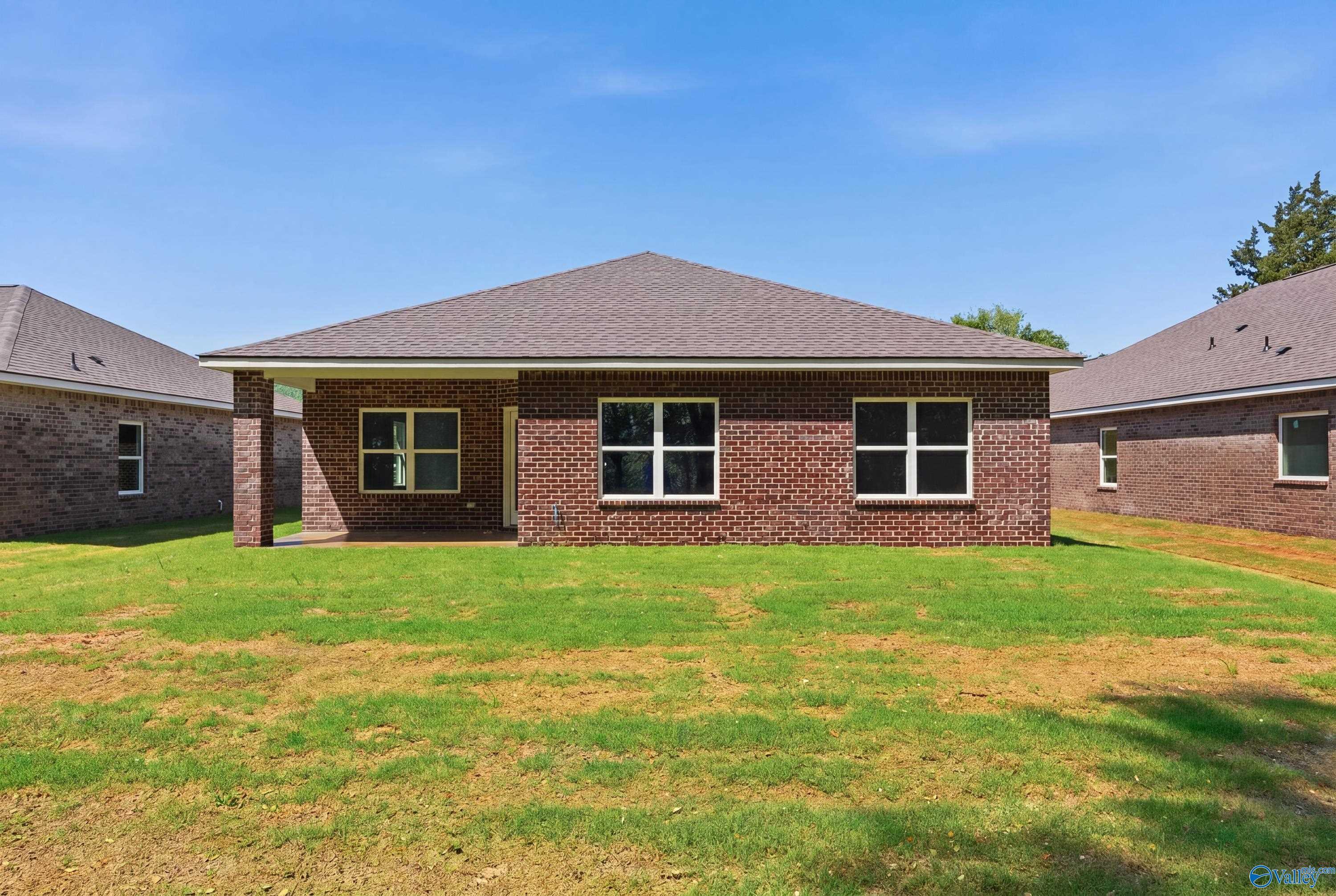 Single-story brick home exterior with covered patio, large windows, and lush green yard in Jaguar Hills, Huntsville, Alabama - The Franklin by Davidson Homes