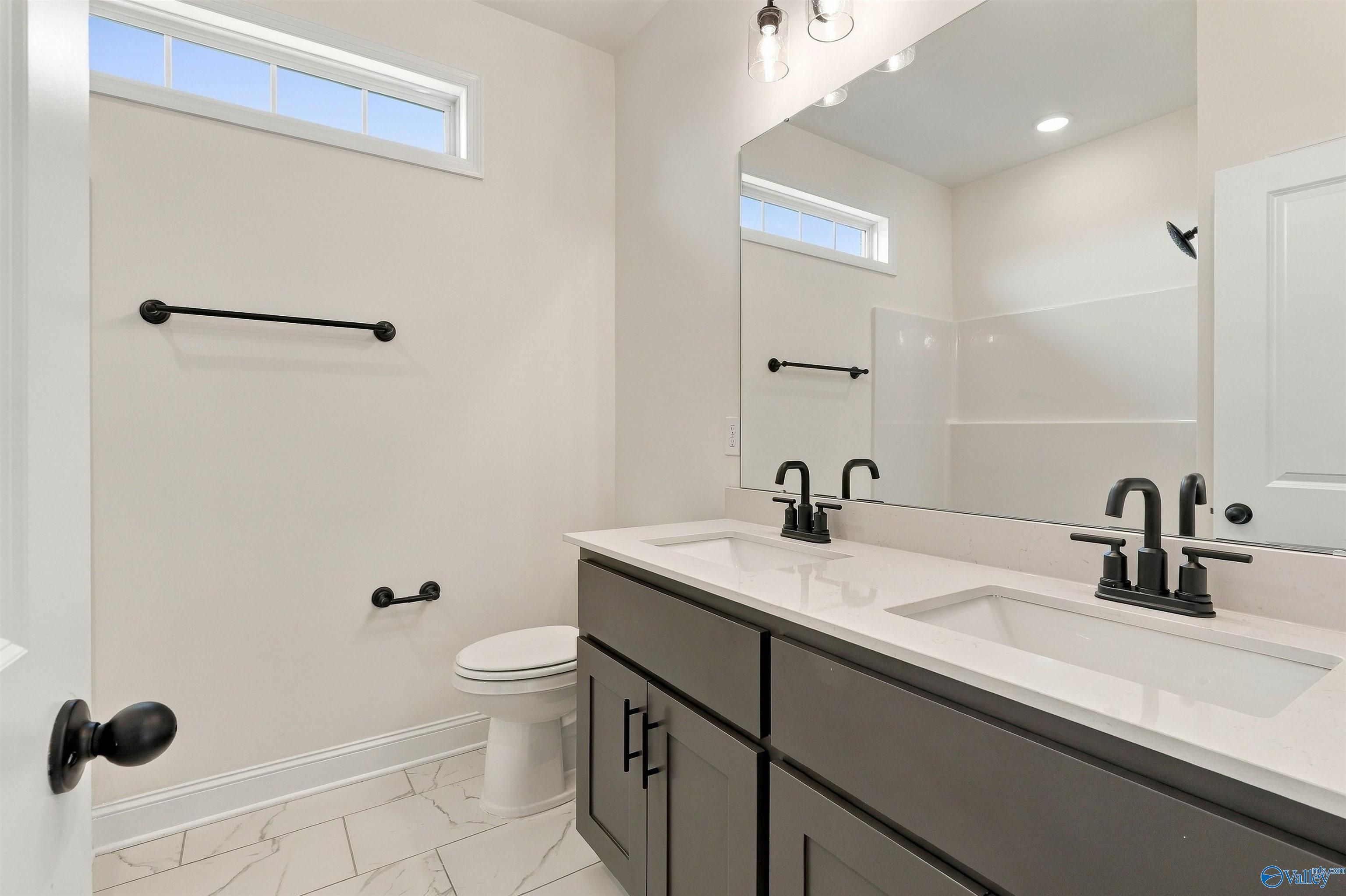 Modern bathroom with dual vanities, matte black fixtures, and marble tile flooring in Davidson Homes The Valencia, Huntsville, AL