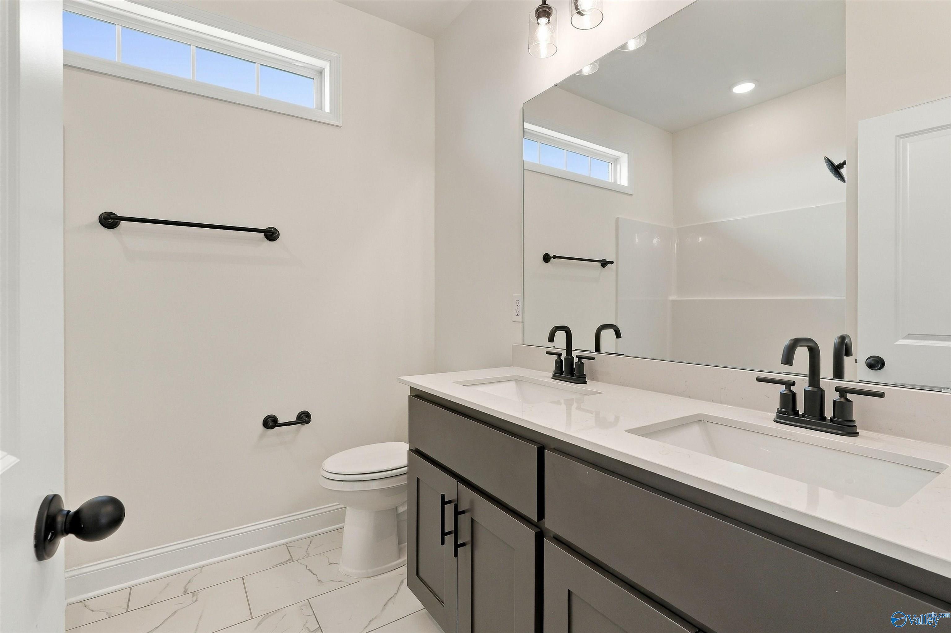 Modern bathroom with dual vanities, matte black fixtures, and marble tile flooring in Davidson Homes The Valencia, Huntsville, AL