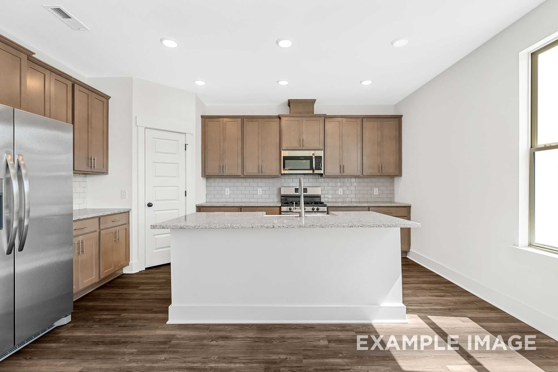 Modern kitchen in The Logan B home design featuring white quartz island, shaker cabinets, subway tile backsplash, and hardwood floors