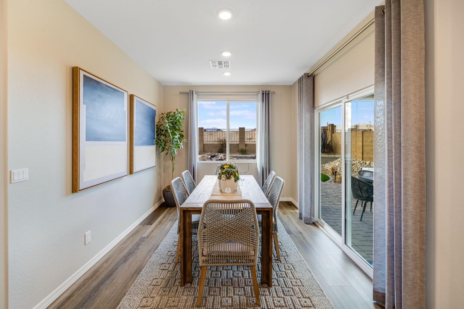 Spacious dining room in The Newport home with rectangular wooden table, rattan chairs, floral centerpiece, sliding doors to patio, neutral tones