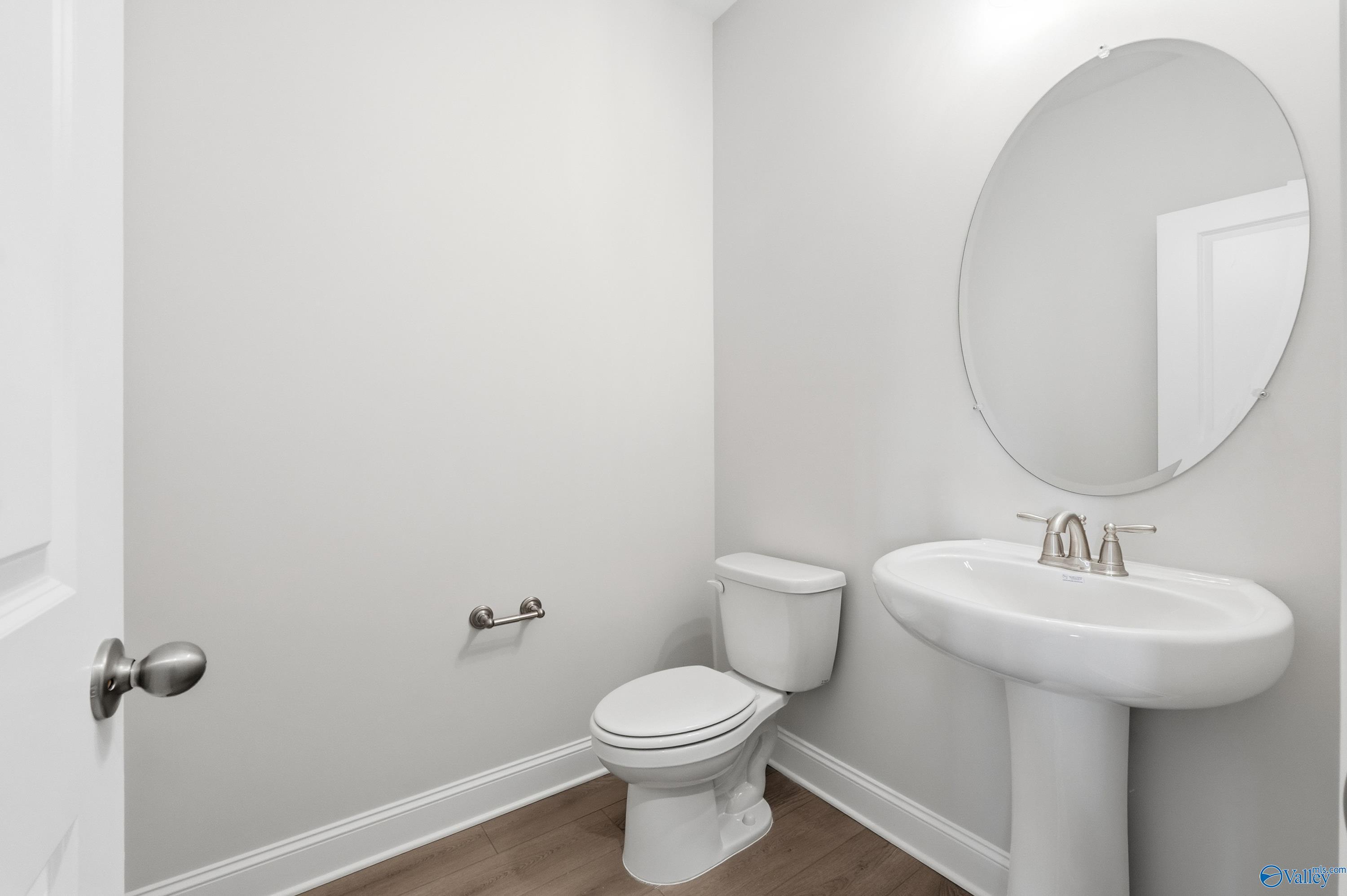 Compact powder room with round mirror, pedestal sink, chrome faucet, and white toilet in Davidson Homes The Finleigh, Creekside, Harvest, Alabama