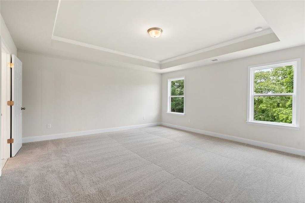 Bright empty bedroom with tray ceiling, neutral walls, carpet floor, and tree-view windows in Davidson Homes The Willow D, Wehunt Meadows, Hoschton
