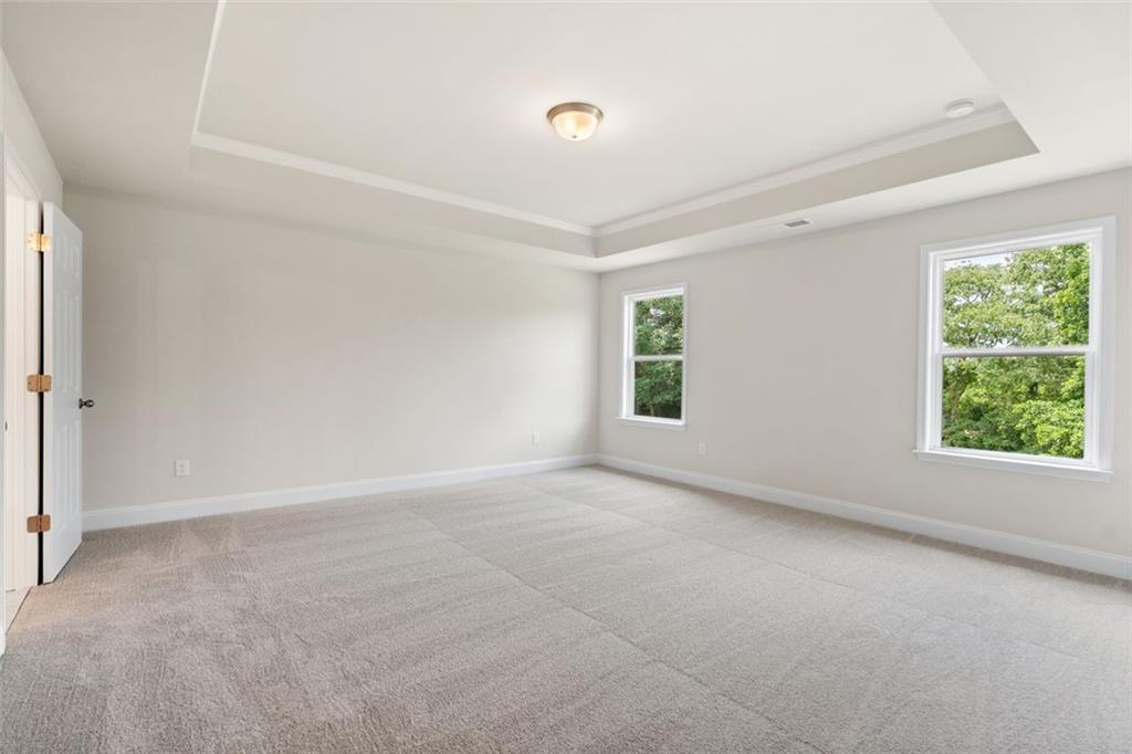 Bright empty bedroom with tray ceiling, neutral walls, carpet floor, and tree-view windows in Davidson Homes The Willow D, Wehunt Meadows, Hoschton