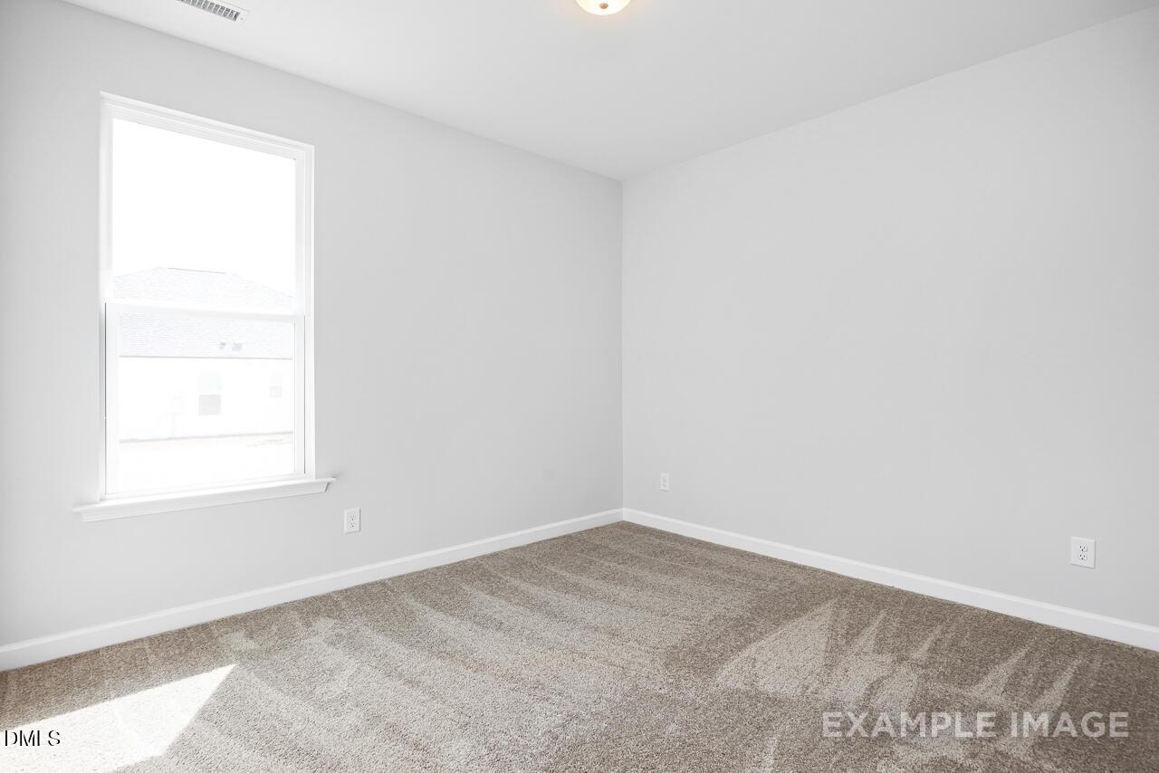 Bright empty bedroom with light gray walls, large sunny window, and beige carpet in Davidson Homes The Daphne C, Zebulon, NC