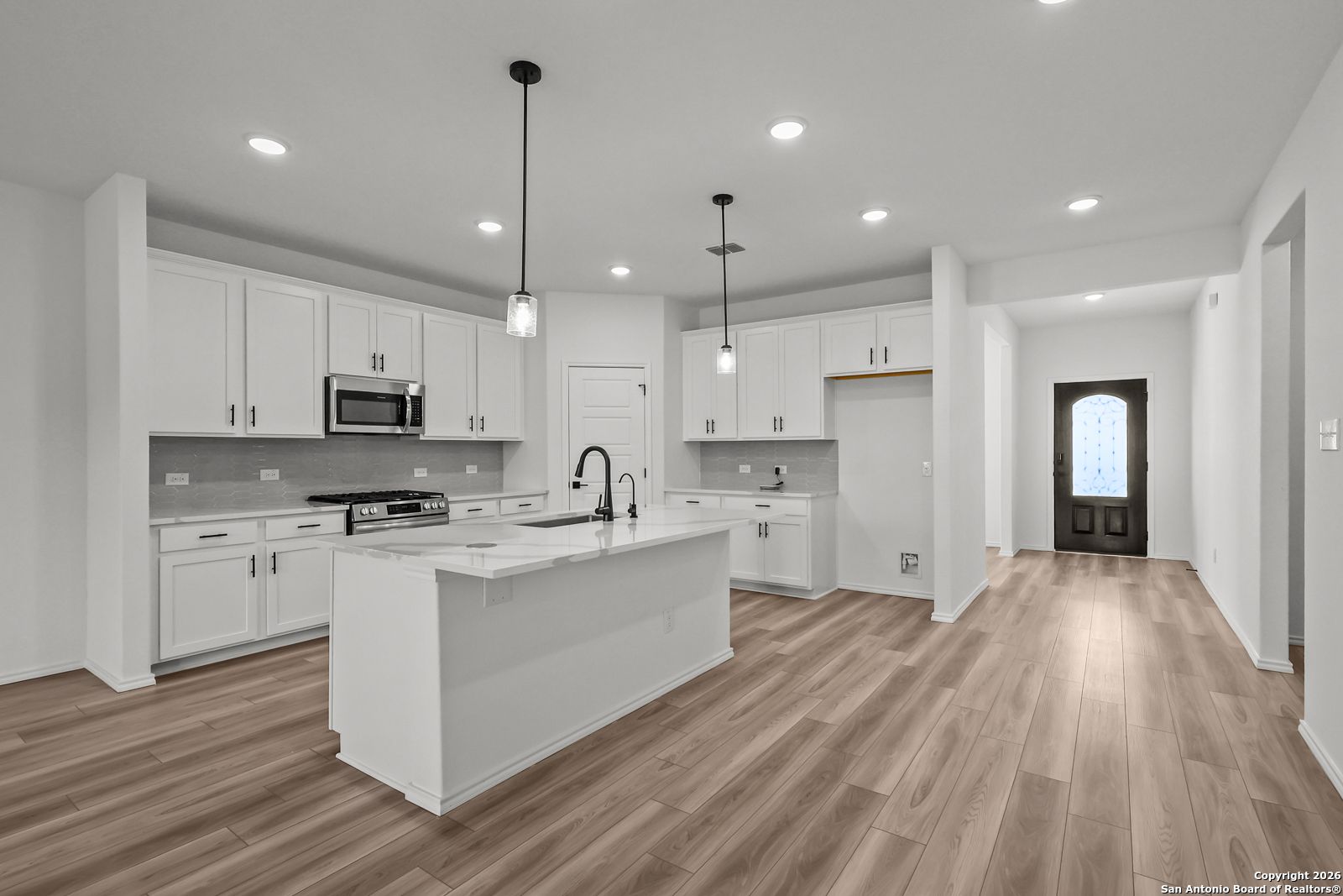 Modern white kitchen featuring large island, stainless appliances, pendant lights in Davidson Homes The Douglas E, San Antonio, Texas