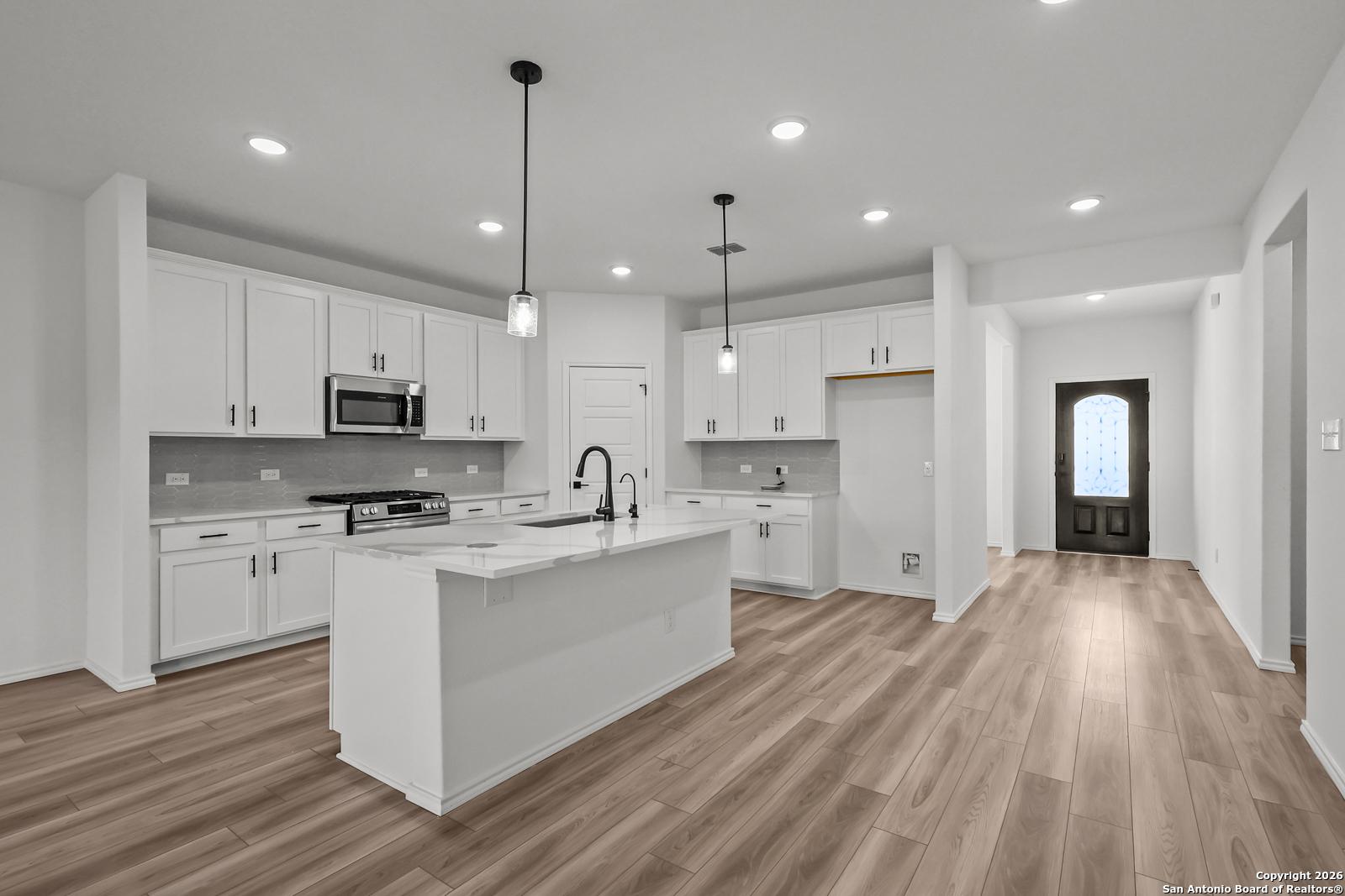 Modern white kitchen featuring large island, stainless appliances, pendant lights in Davidson Homes The Douglas E, San Antonio, Texas