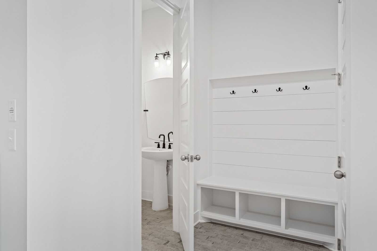 White mudroom with built-in bench, coat hooks, and adjacent laundry room pedestal sink in The Alston A, Murfreesboro, TN