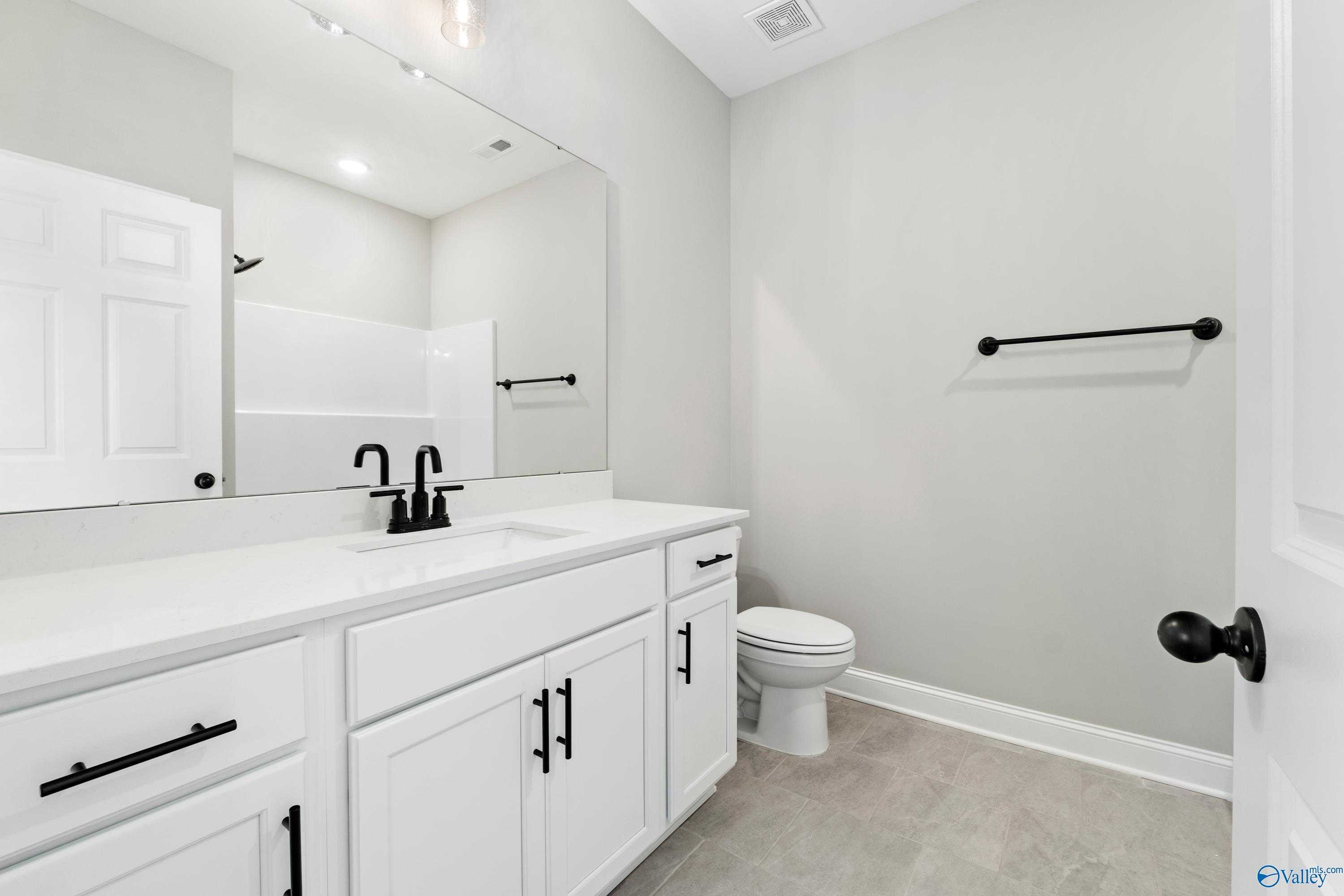 Elegant bathroom with white vanity, black faucet, large mirror, and walk-in shower in Davidson Homes The Valencia, Meridianville, AL