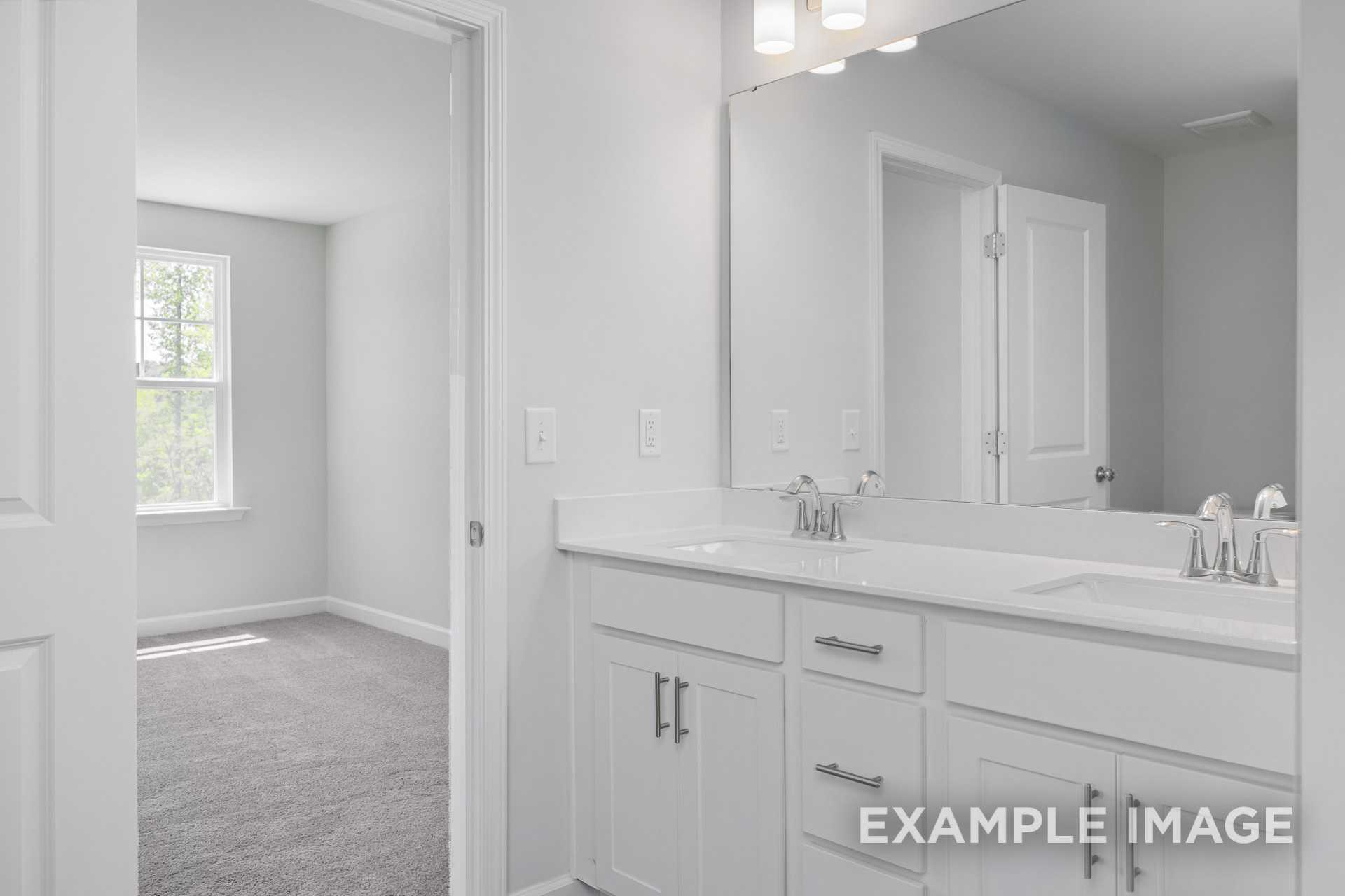 Spacious master bathroom in The Gavin C by Davidson Homes featuring white double vanity, large mirror, and adjacent carpeted bedroom