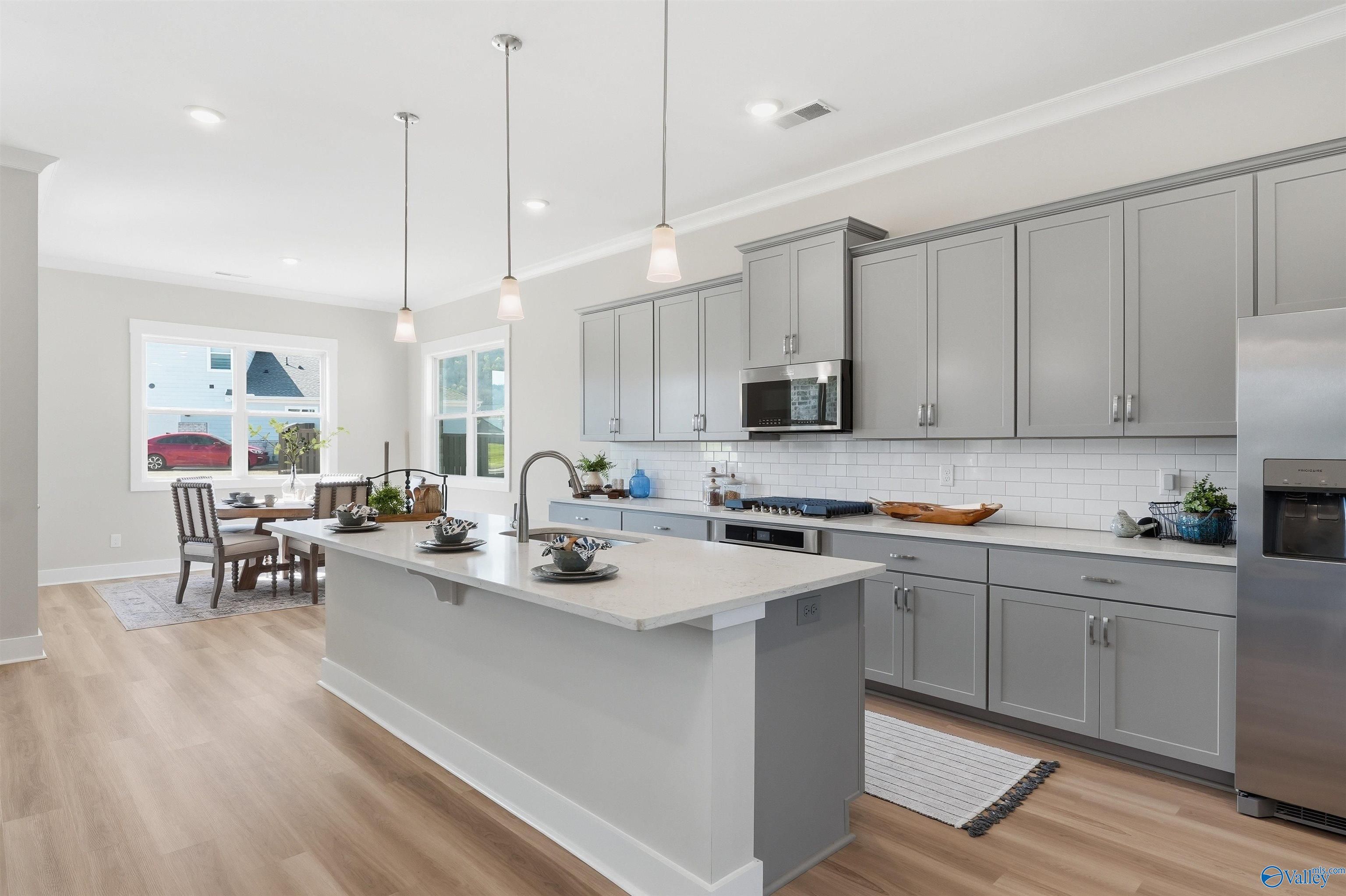 Open-concept kitchen with gray shaker cabinets, quartz island, stainless appliances, subway tile backsplash in Evermore Homes The Oxford B, Owens Cross Roads