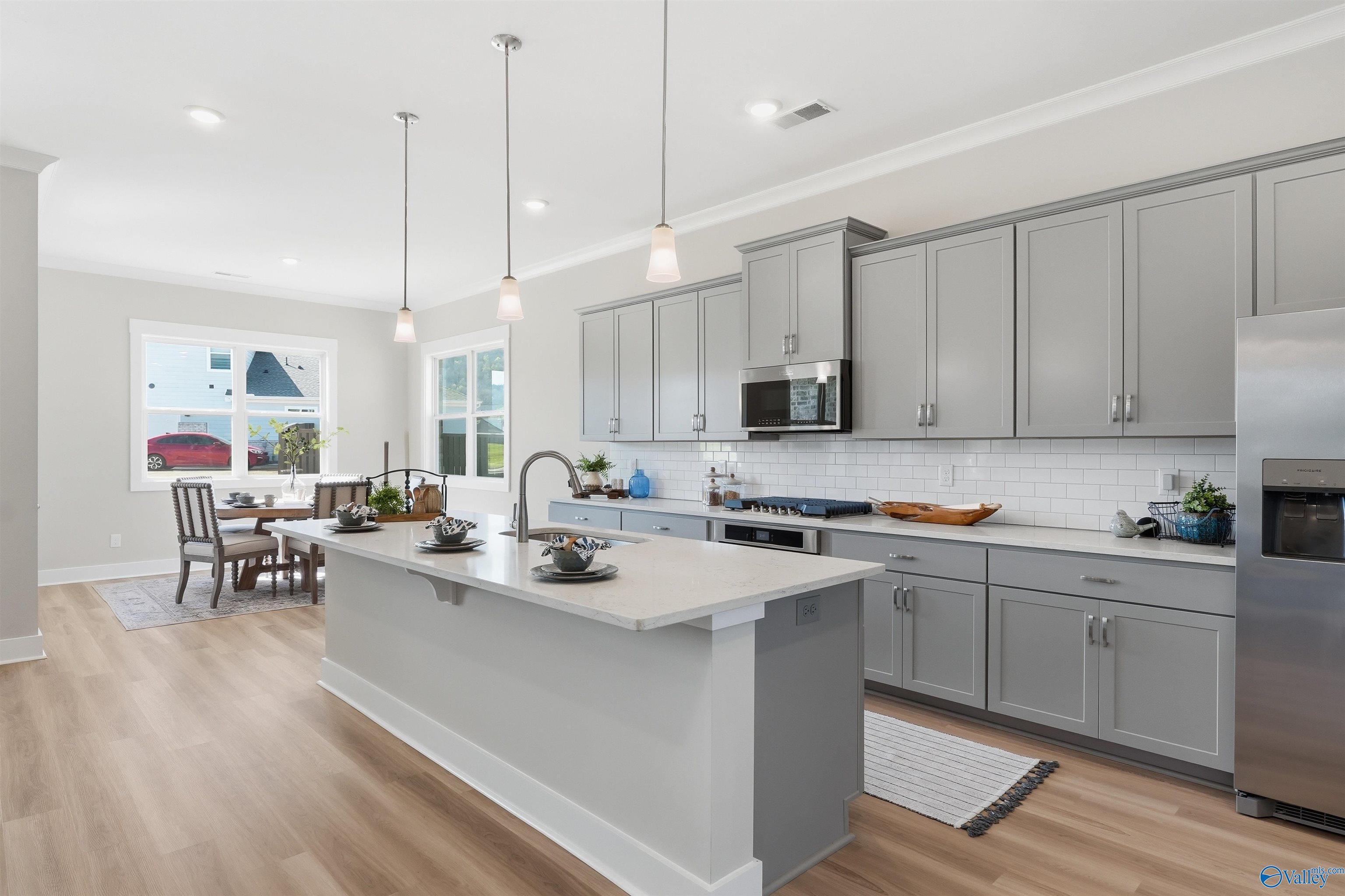 Open-concept kitchen with gray shaker cabinets, quartz island, stainless appliances, subway tile backsplash in Evermore Homes The Oxford B, Owens Cross Roads