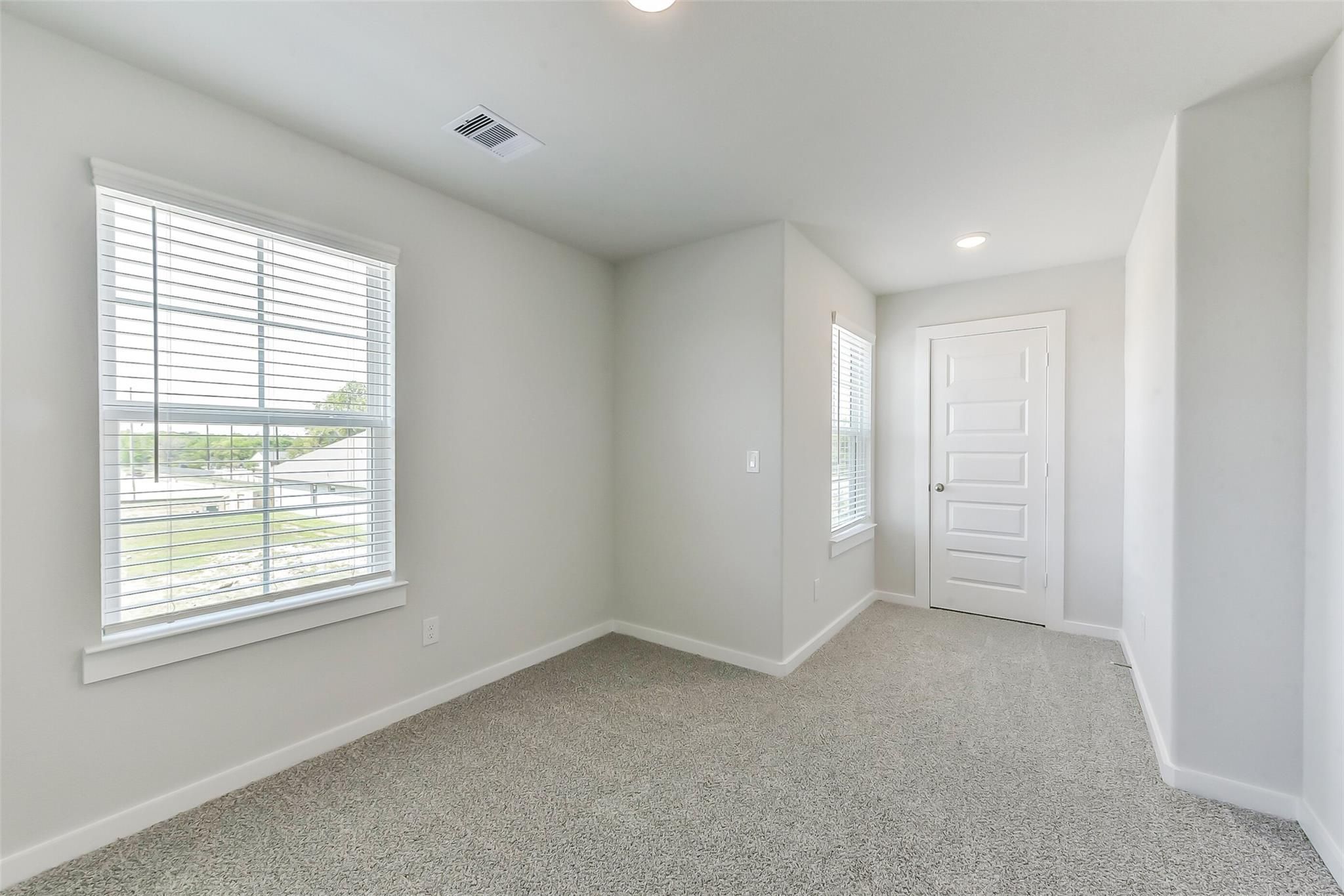 Bright empty bedroom featuring light gray walls, white window blinds, gray carpet, and white door in Davidson Homes The Brazos E, Magnolia, Texas