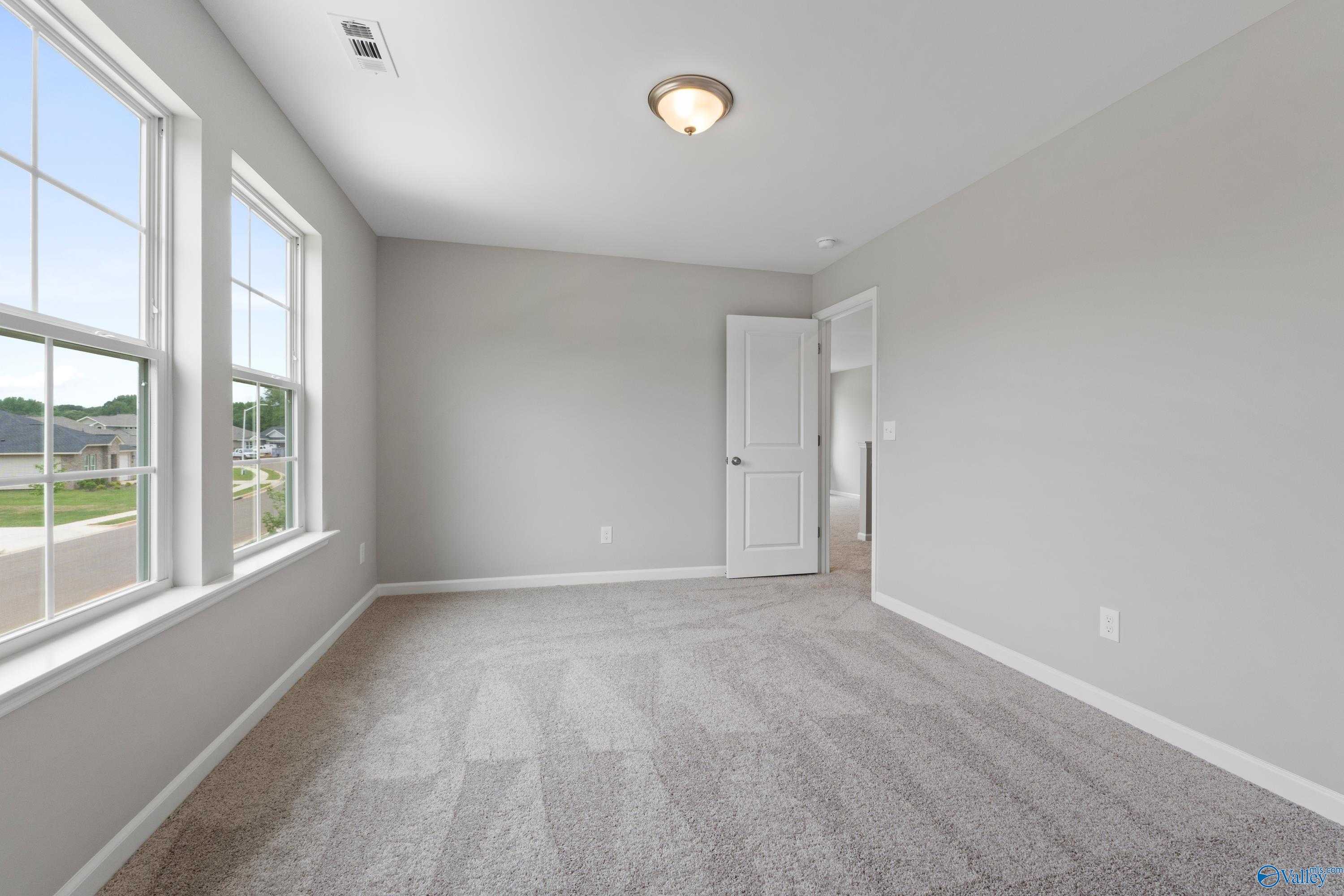 Bright empty bedroom with light gray walls, large windows, carpet floor in Davidson Homes The Stella, Hazel Green, AL