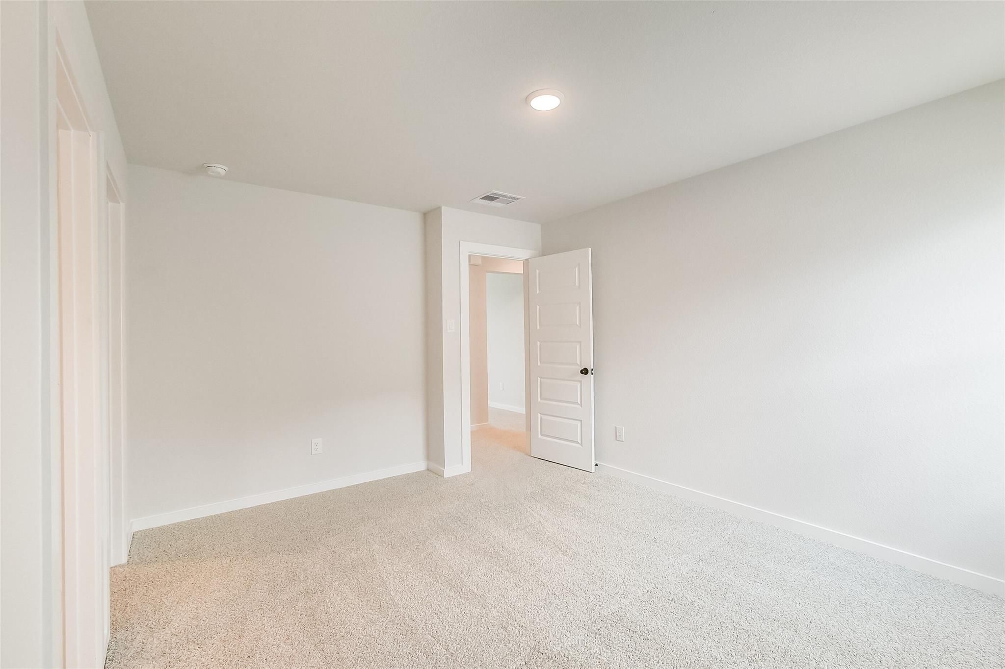 Spacious empty bedroom with beige carpet, light gray walls, and open door to bath in Davidson Homes Tierra B, Beasley TX