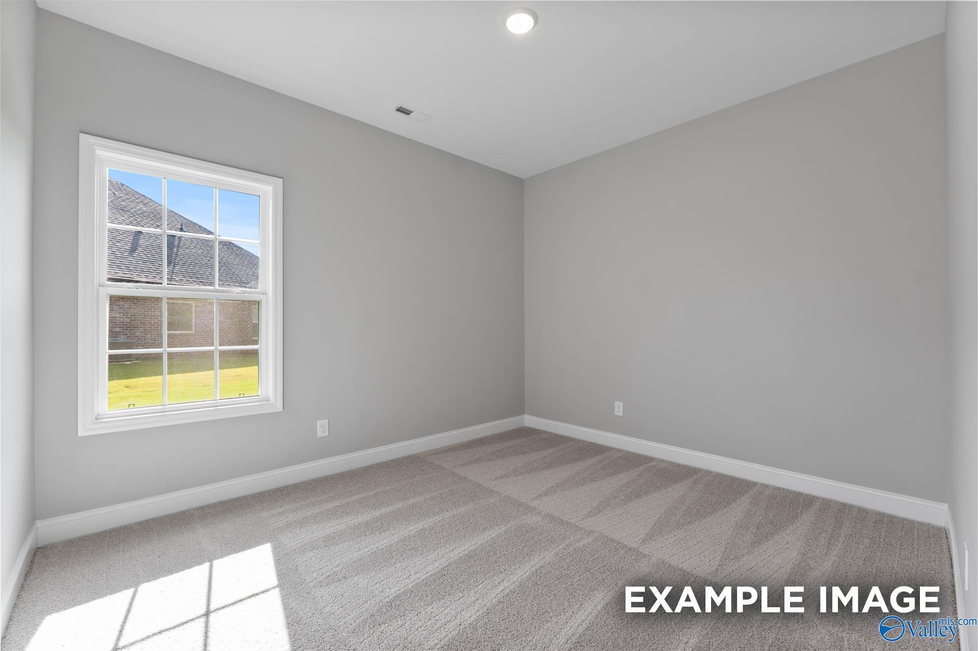 Sunlit empty secondary bedroom with light gray walls, carpeted floor, and large window in Davidson Homes The Rockford with Bonus, Madison Alabama